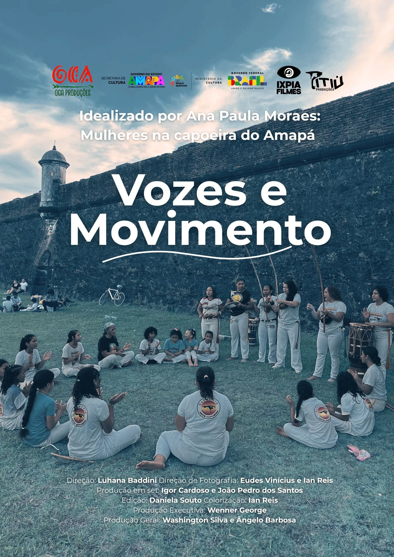 Grupo de mulheres e crianças participando de uma atividade cultural ao ar livre, com uma parede de pedra ao fundo