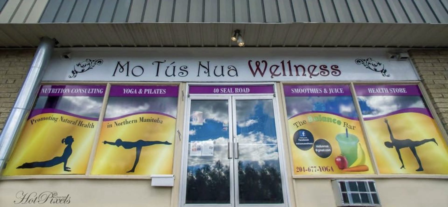 Storefront window for Mo Tús Nua Wellness, offering nutrition consulting, yoga, Pilates, smoothies, juice, and health store products, with signs and graphics promoting natural health and yoga poses.