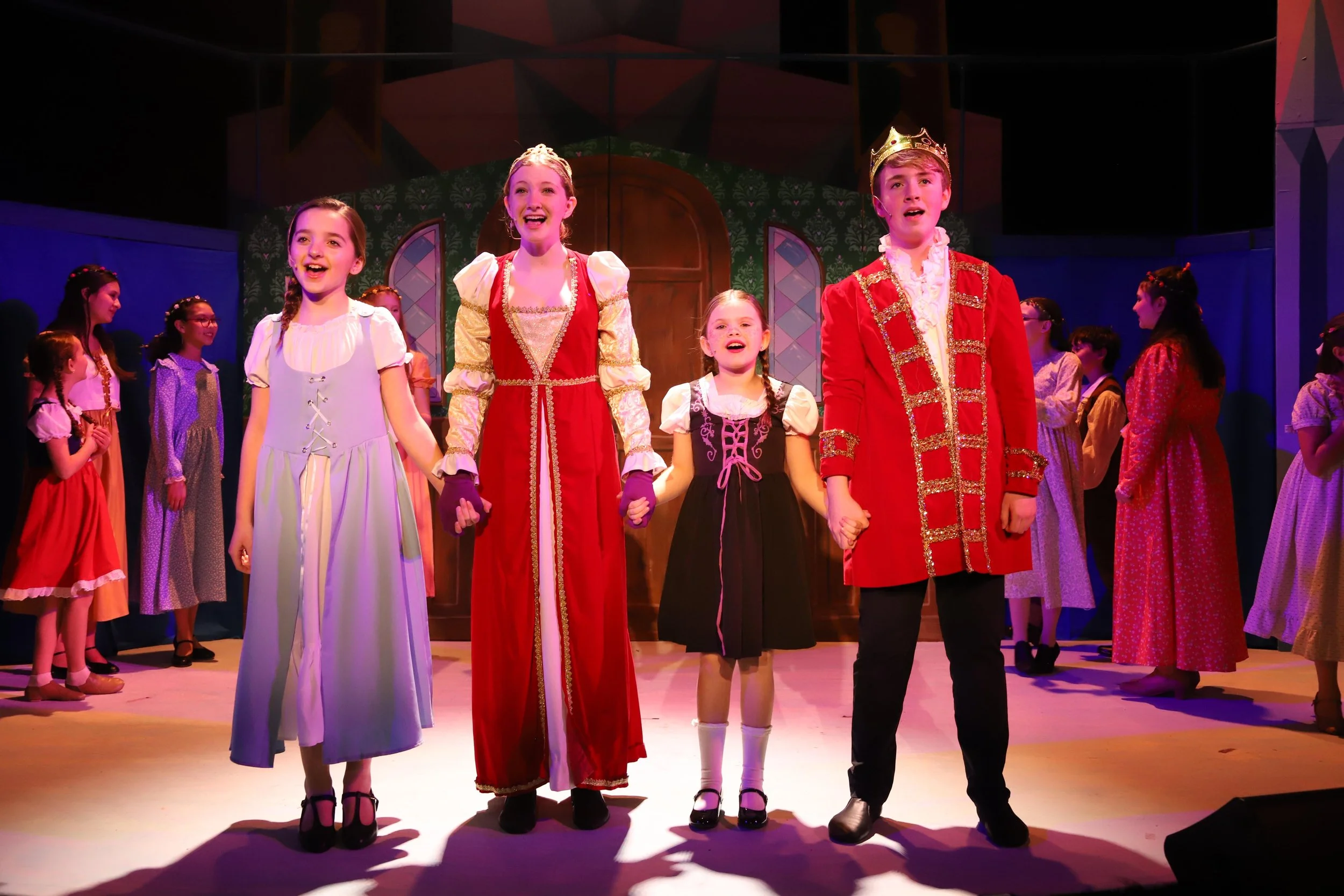 Kids performing in Frozen Jr. dressed as princes, princesses, and other fairy tale characters, holding hands and taking a bow.