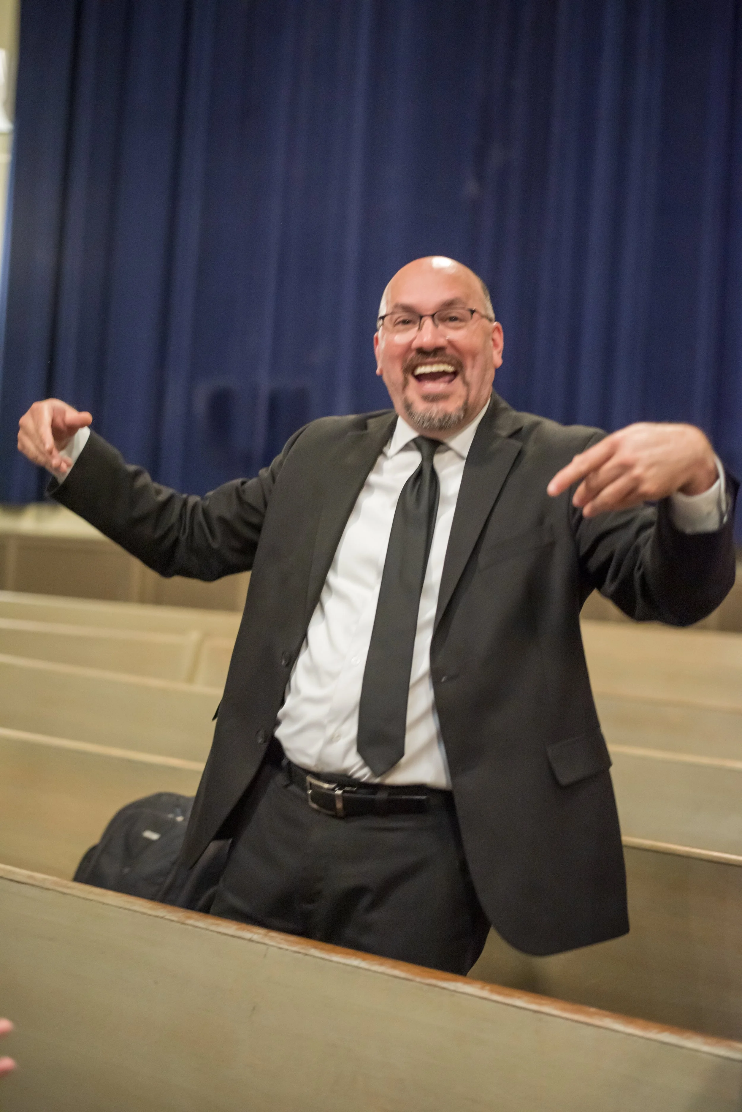 A man in a suit smiling and gesturing excitedly at Grandma Sylvia's Funeral.