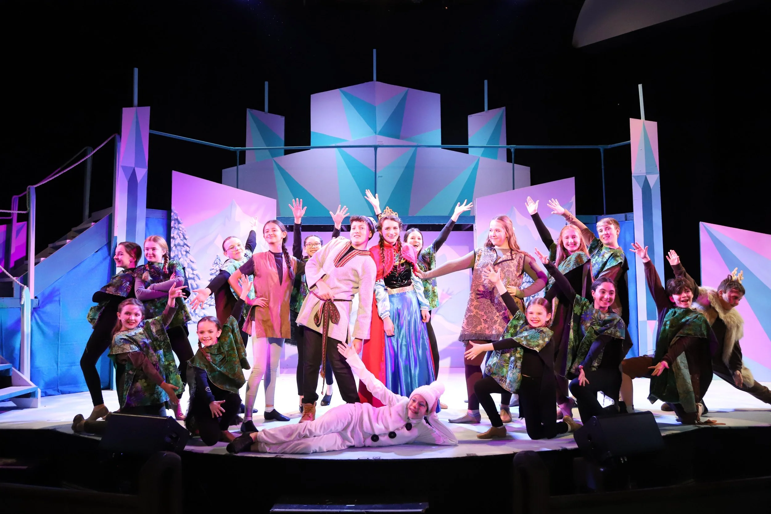 Children in colorful costumes performing on stage in a theatrical production of Frozen Jr.