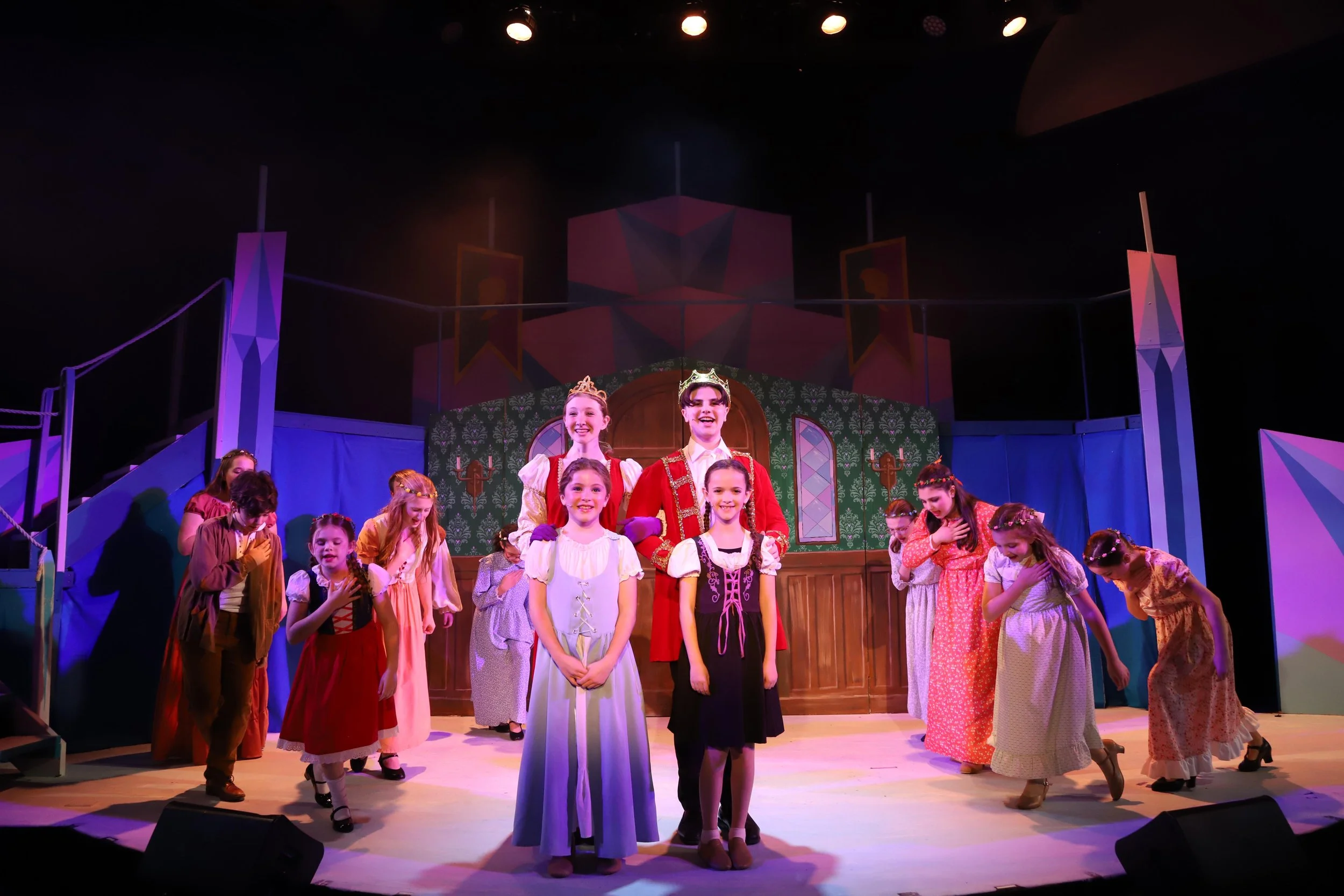The cast of a theatrical play on stage, dressed in costumes of princes and princesses, taking a bow after their performance.