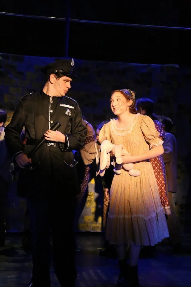 A young policeman and a girl in a yellow dress sharing a moment during a stage performance.