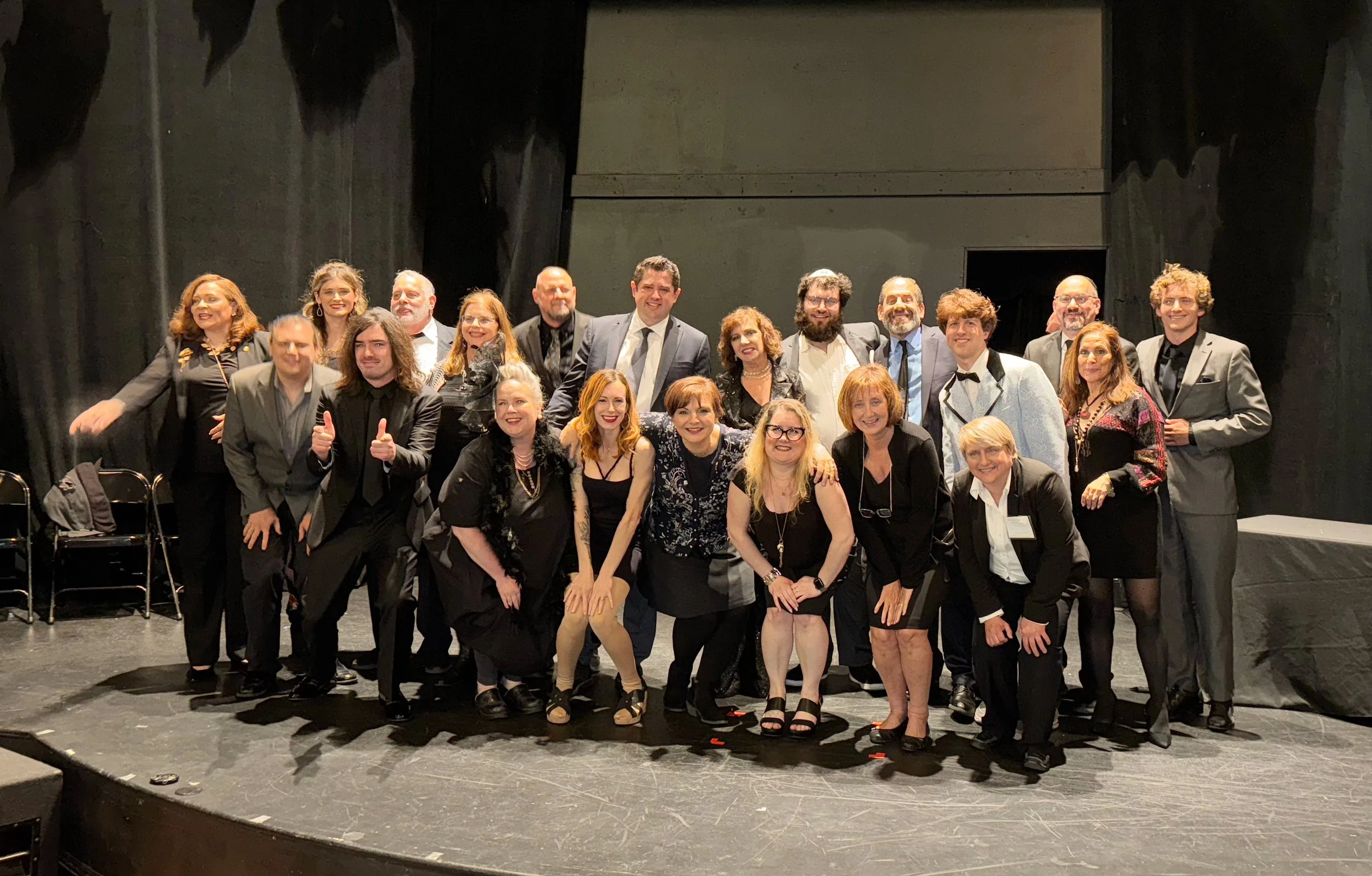 Cast of 18 people on a stage, dressed formally, smiling and posing together after Grandma Sylvia's Funeral.