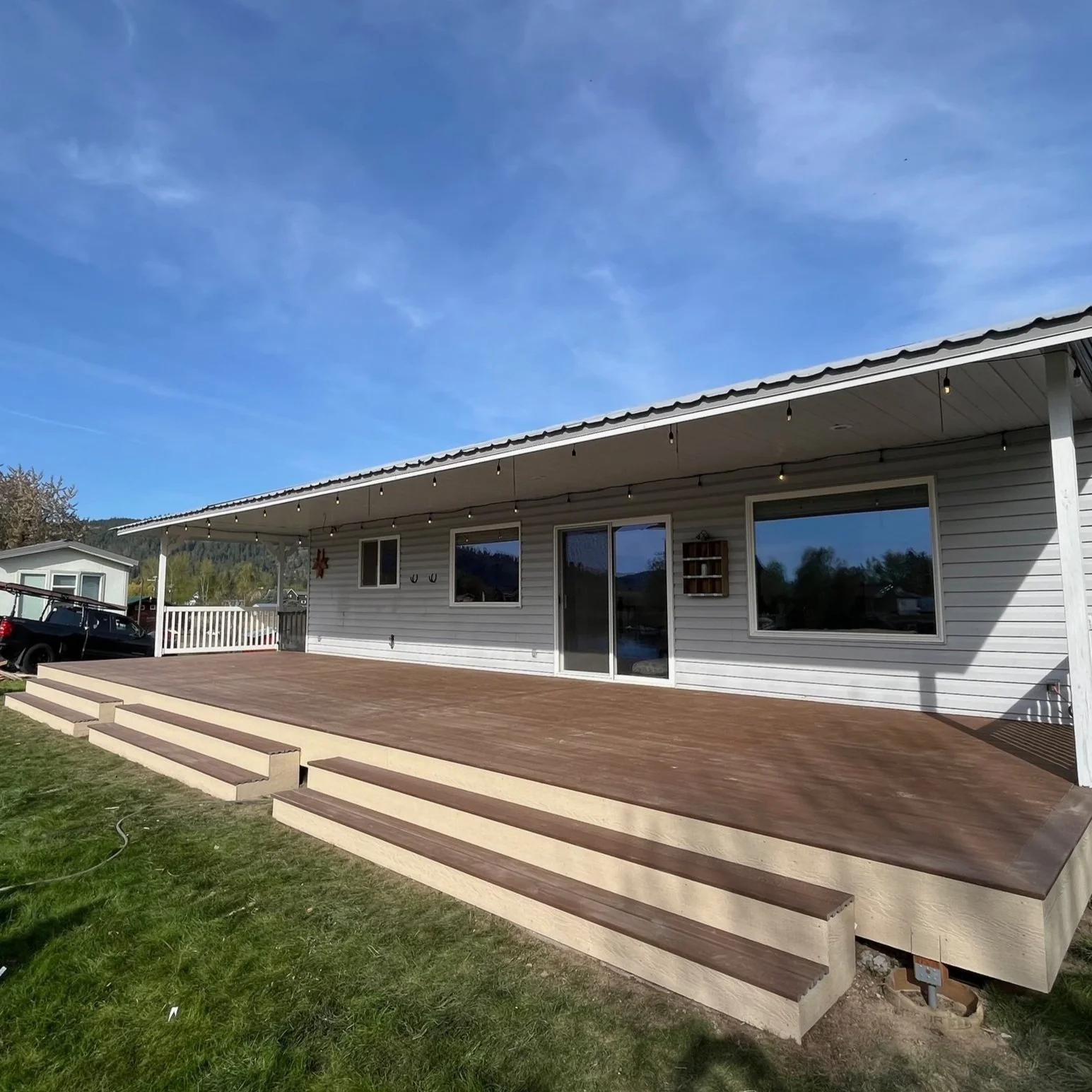 A house with a newly built wooden deck and steps, white siding, sliding glass door, and large windows, under a clear blue sky.