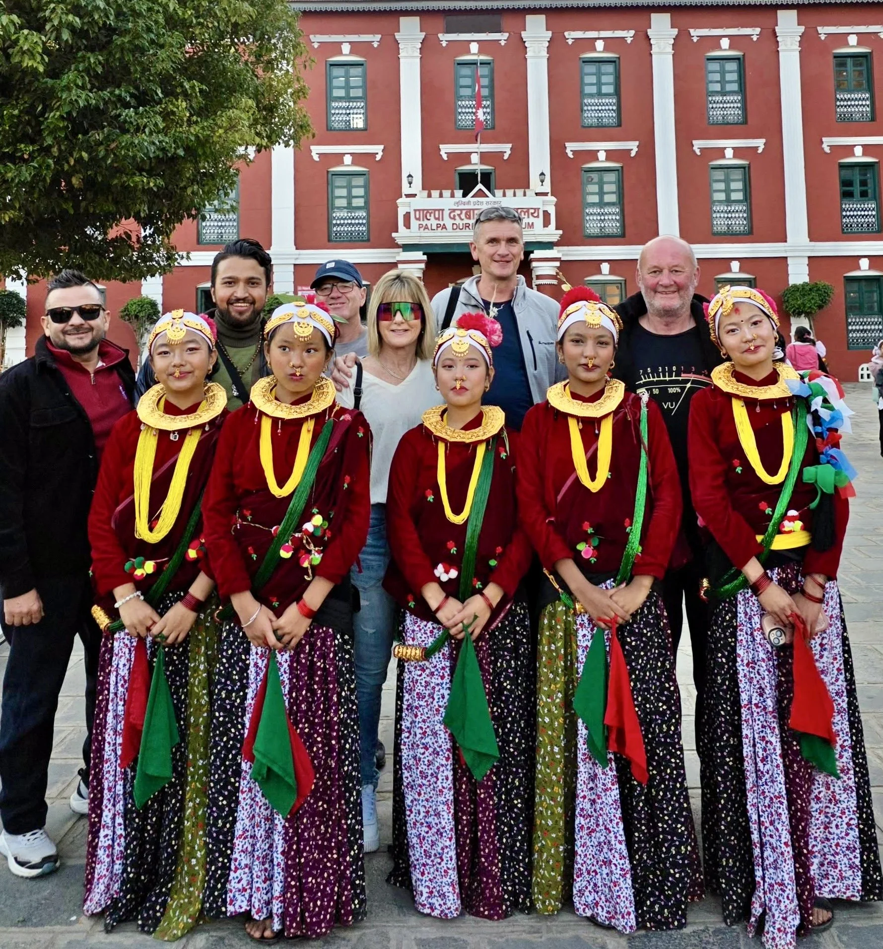 A group of tourists with local performers dressed in traditional attire standing in front of the Palpa Durbar Museum in Nepal.