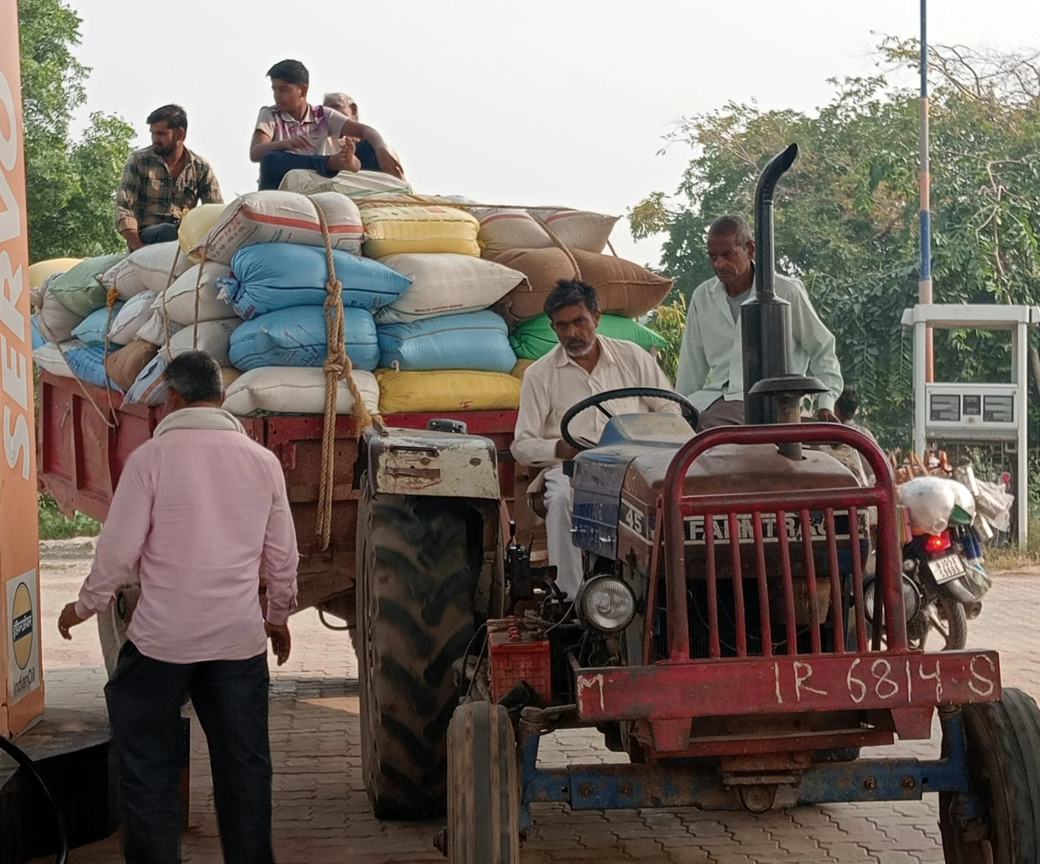 People loading bags onto a truck via tractor in an outdoor area.