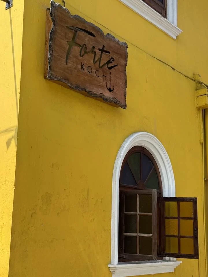 Yellow building with an arched window, one side of the window open, and a sign that reads 'Torte KoChu' mounted on the wall.