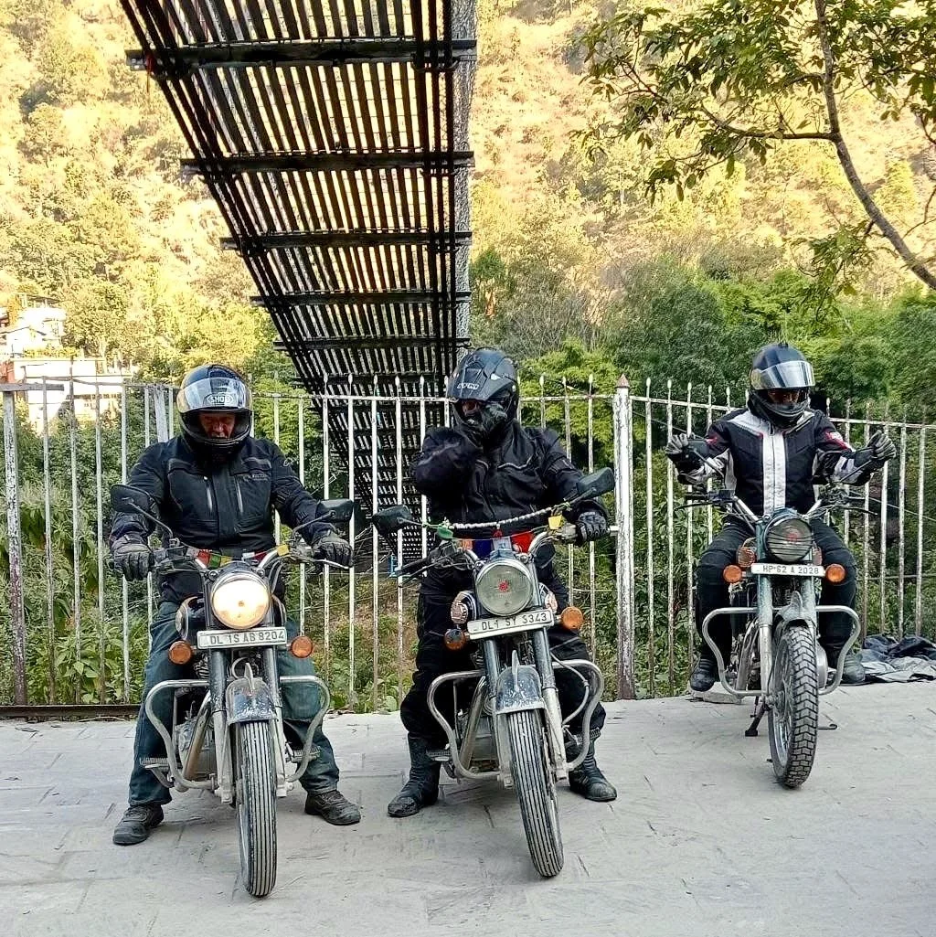 Three motorcyclists dressed in black riding gear, wearing helmets, sitting on their bikes, with a staircase and trees in the background.