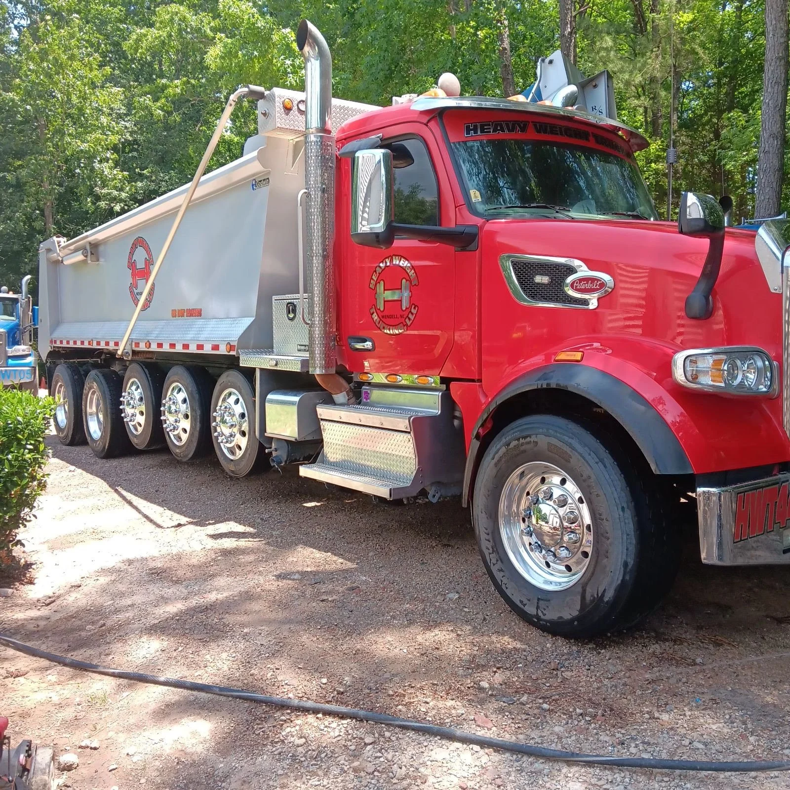 Red heavy-duty fire truck with silver and white equipment, parked on a dirt path surrounded by green trees.