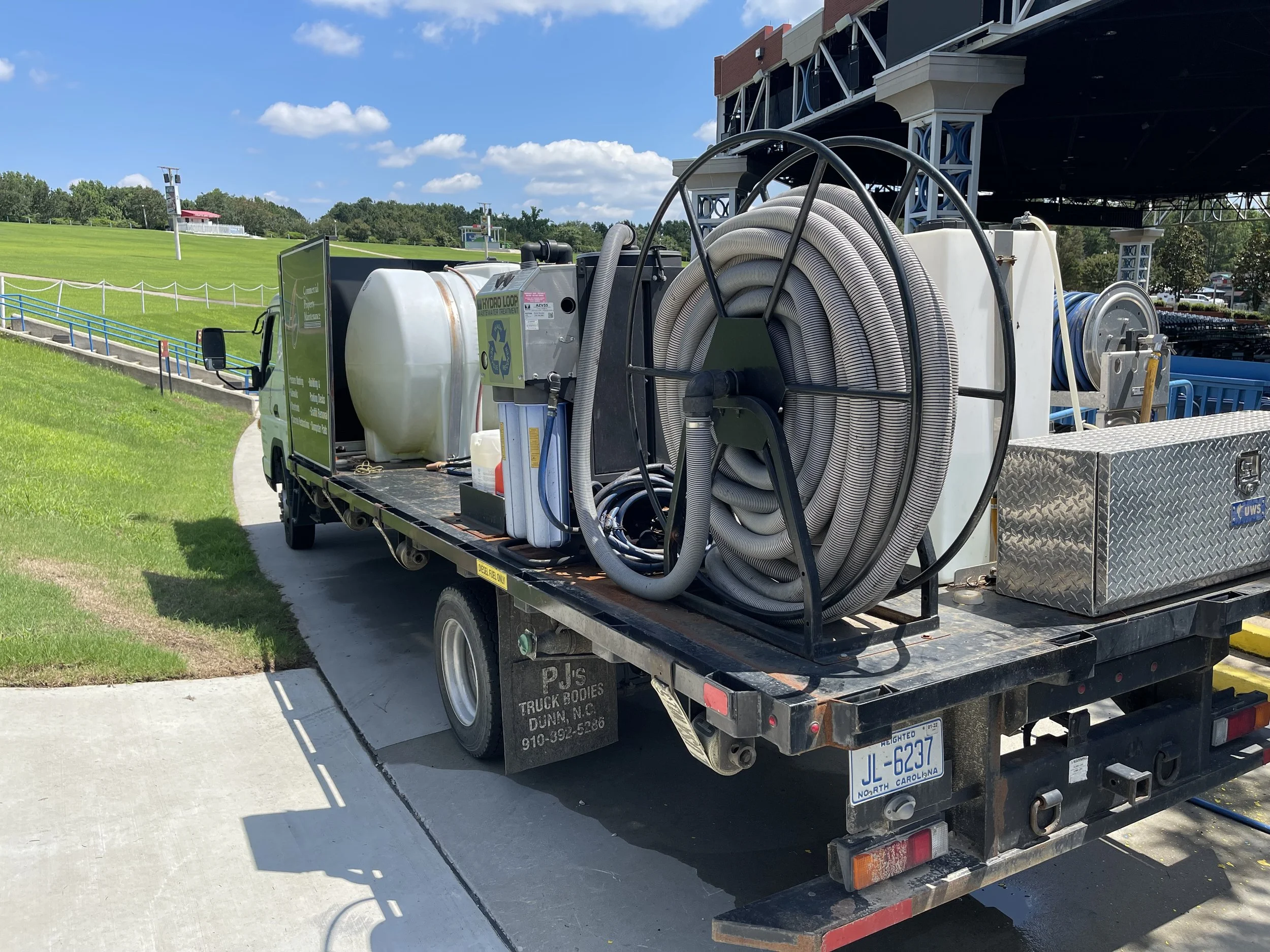 A utility truck parked on a sidewalk, equipped with hoses, a large water tank, and other equipment.
