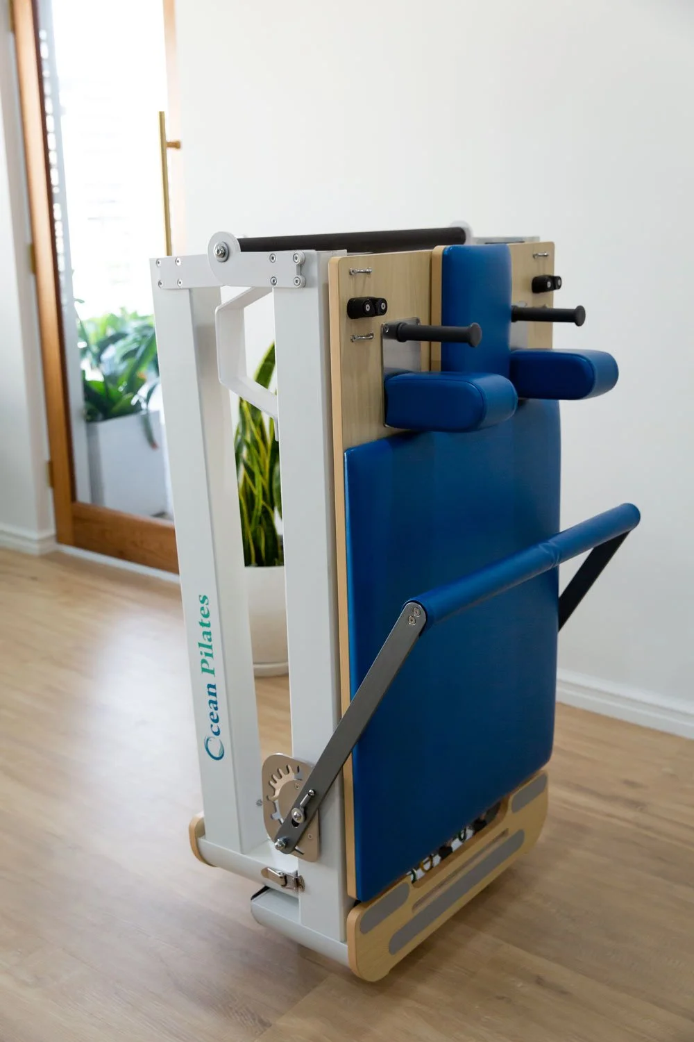 Three-quarter view of the Elite Folding Pilates Reformer folded into upright storage position.