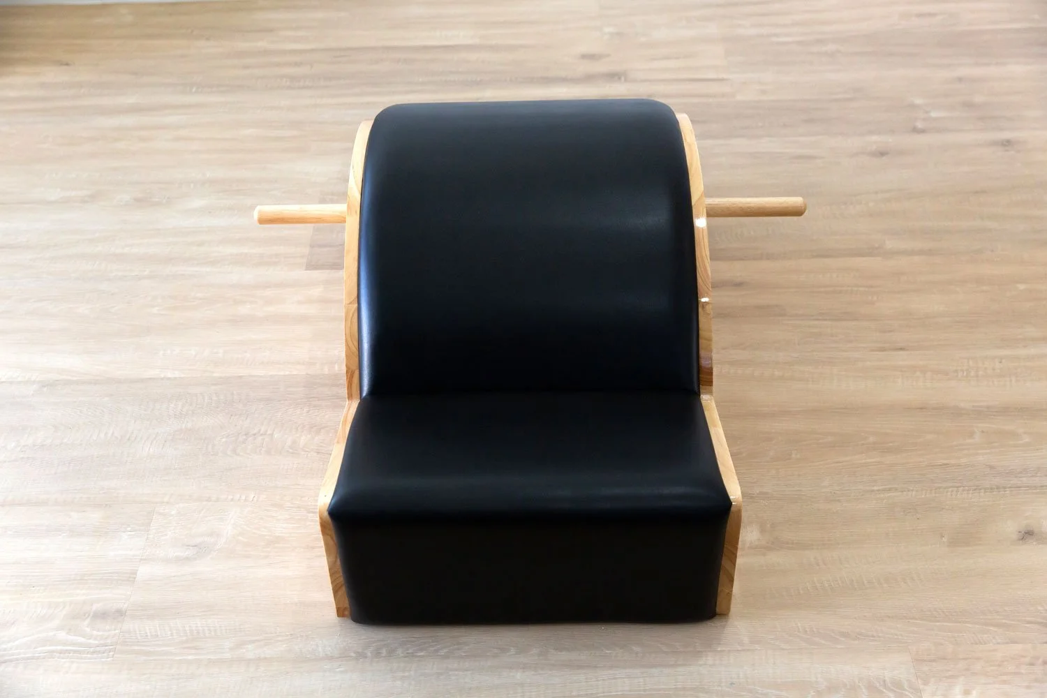 Front view of Pilates spine corrector with black padded surface and wooden dowel.