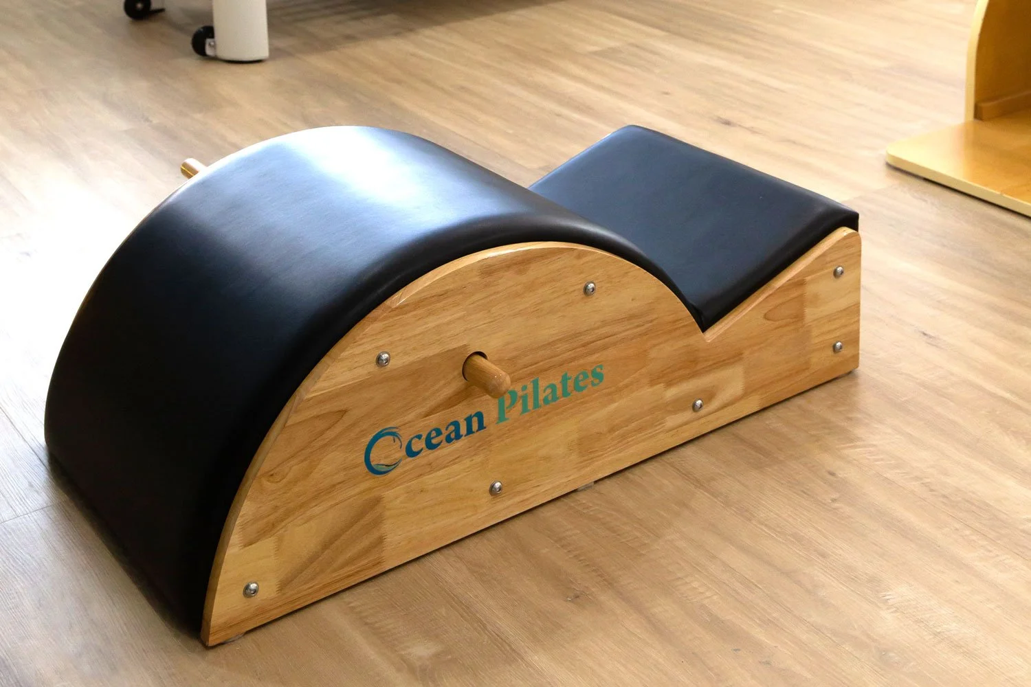 Wooden Pilates spine corrector with black padded arch, angled side view.