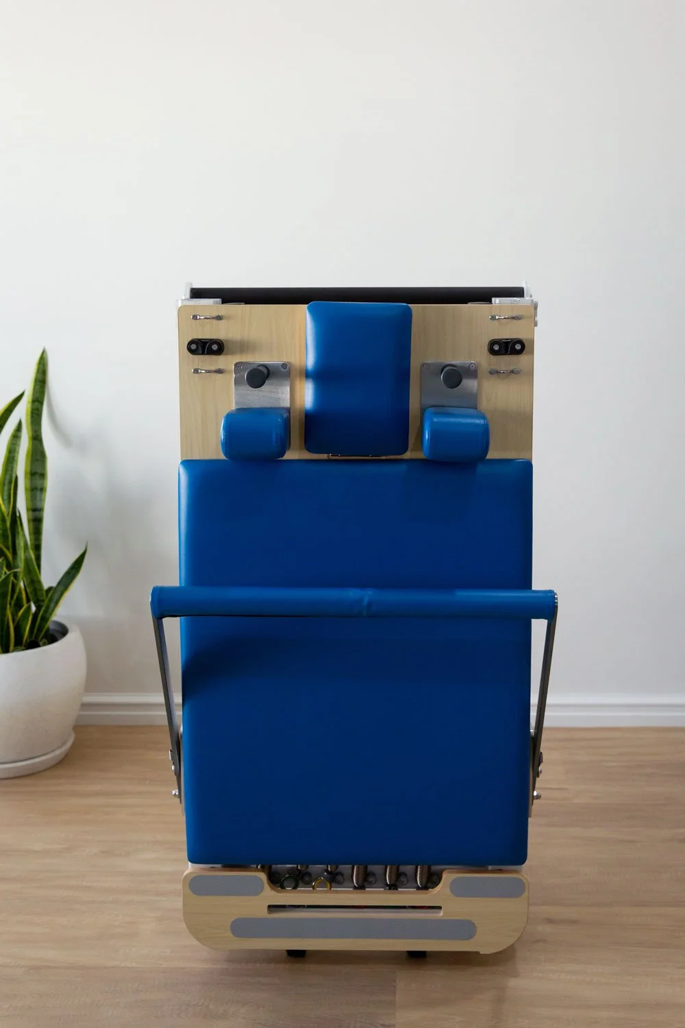Front view of Elite Folding Pilates Reformer in upright storage mode with headrest and foot-bar visible.