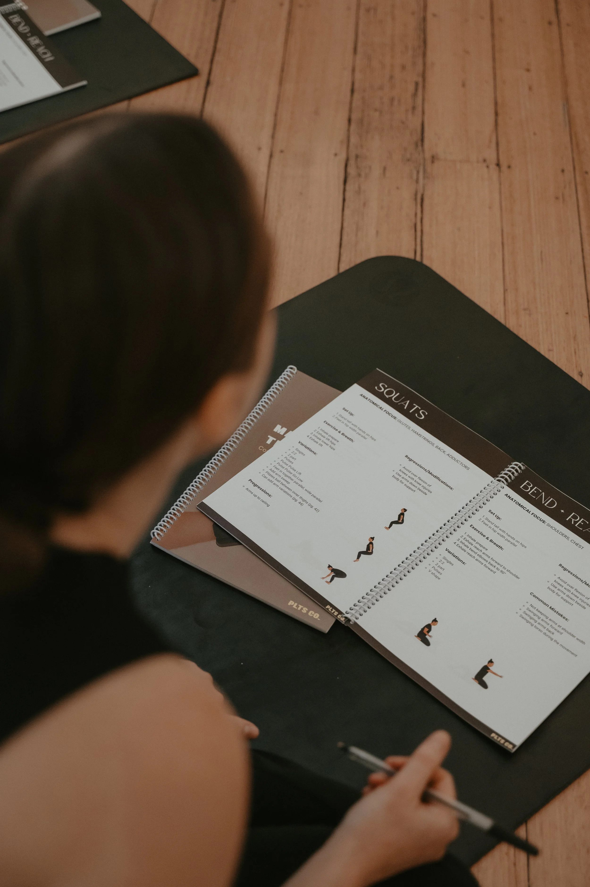 A person sitting on the floor studying pilates exercises from a spiral-bound guide with illustrations and descriptions of pilates exercises.