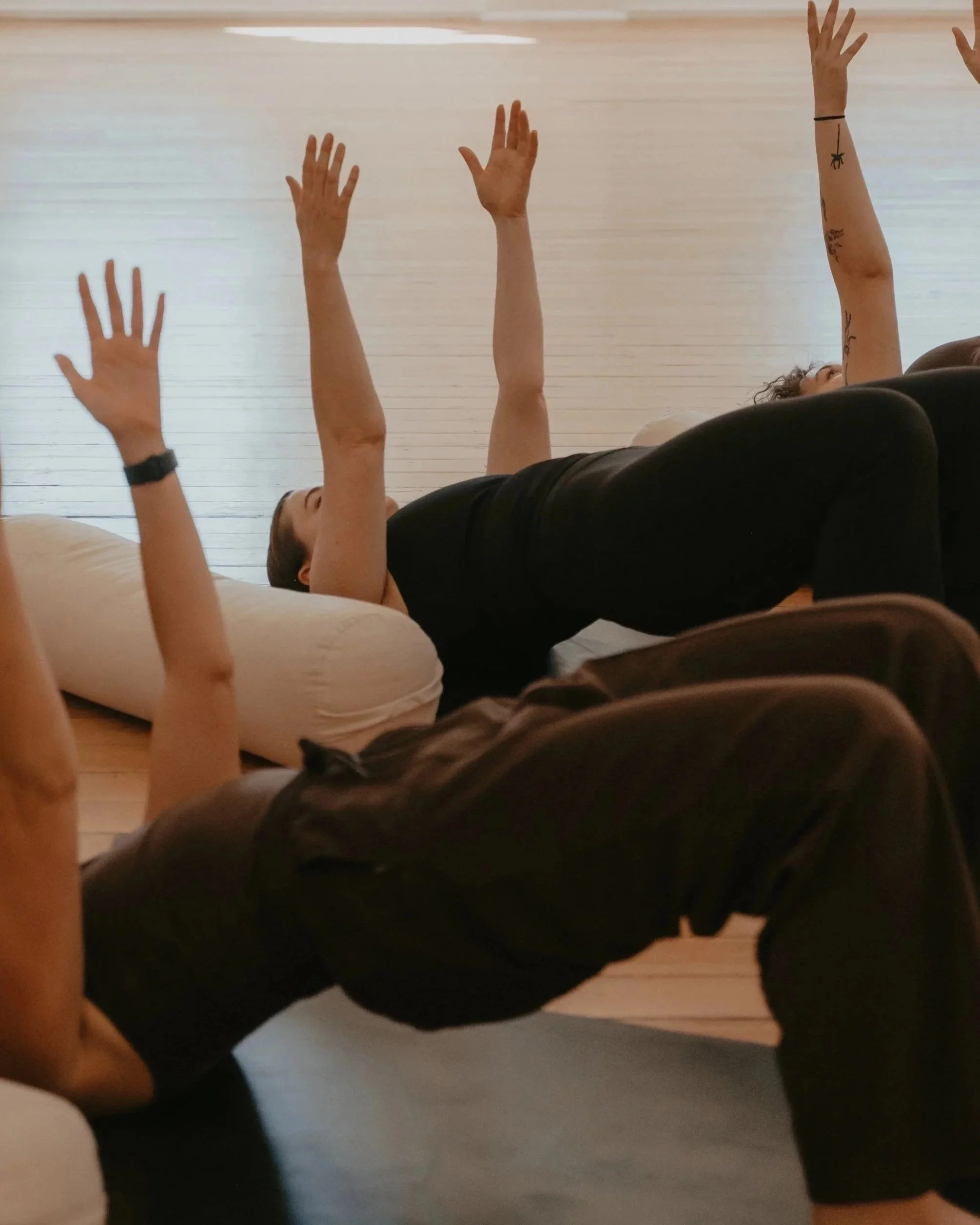 People participating in a pilates class, lying on mats and raising their arms.