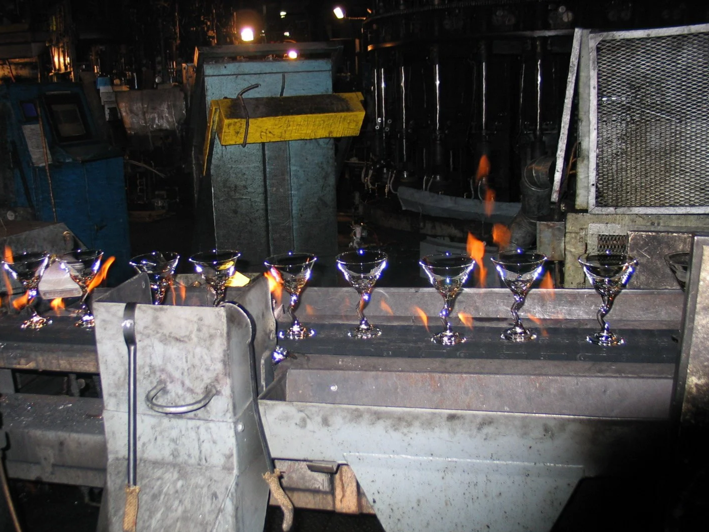 Tableware Glassware on a metal production line with flames from a forging process in a factory setting.