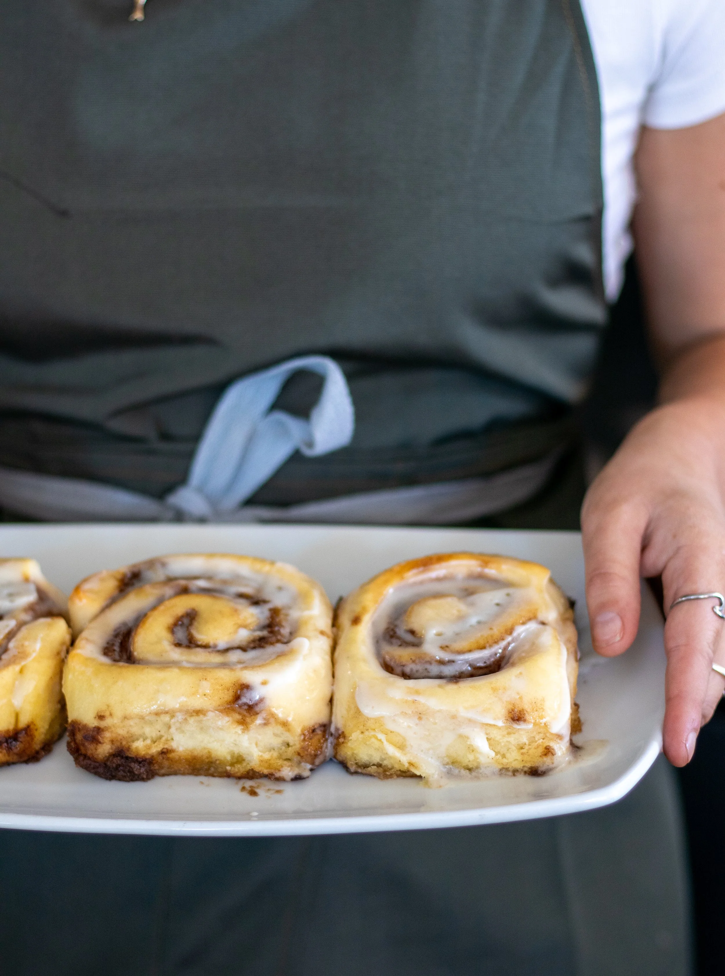 Person holding a white rectangular plate with three cinnamon rolls drizzled with icing.