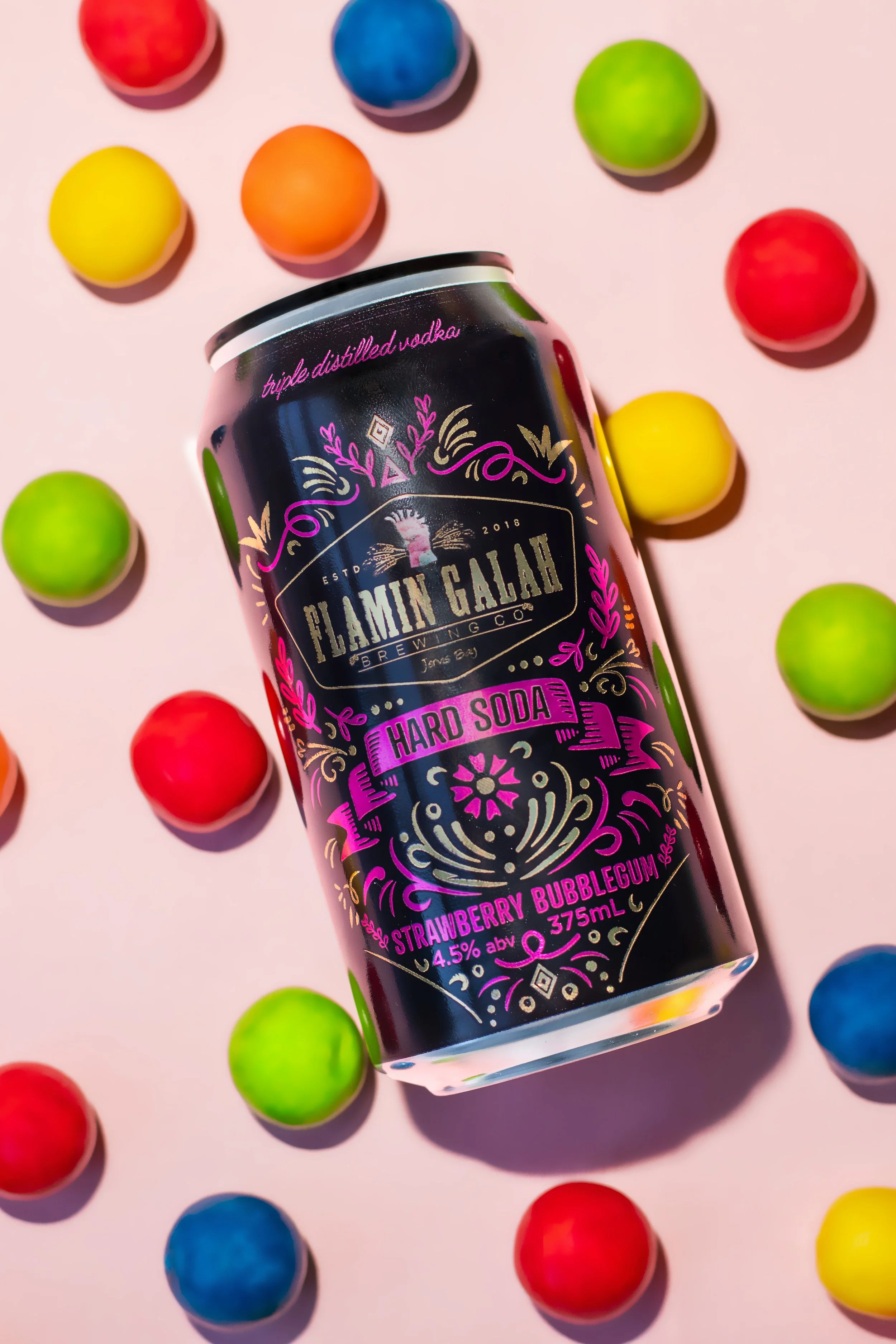 A can of Flaming Gala hard soda with strawberry bubblegum flavor surrounded by colorful gumballs on a pink background.