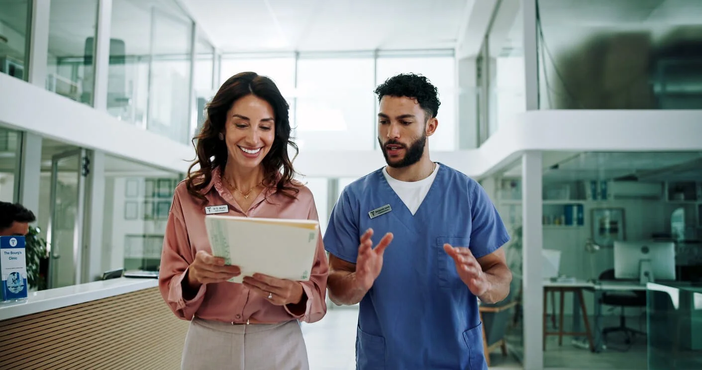 A woman and a man, possibly healthcare professionals, are standing together in a modern medical facility, looking at a folder and discussing.