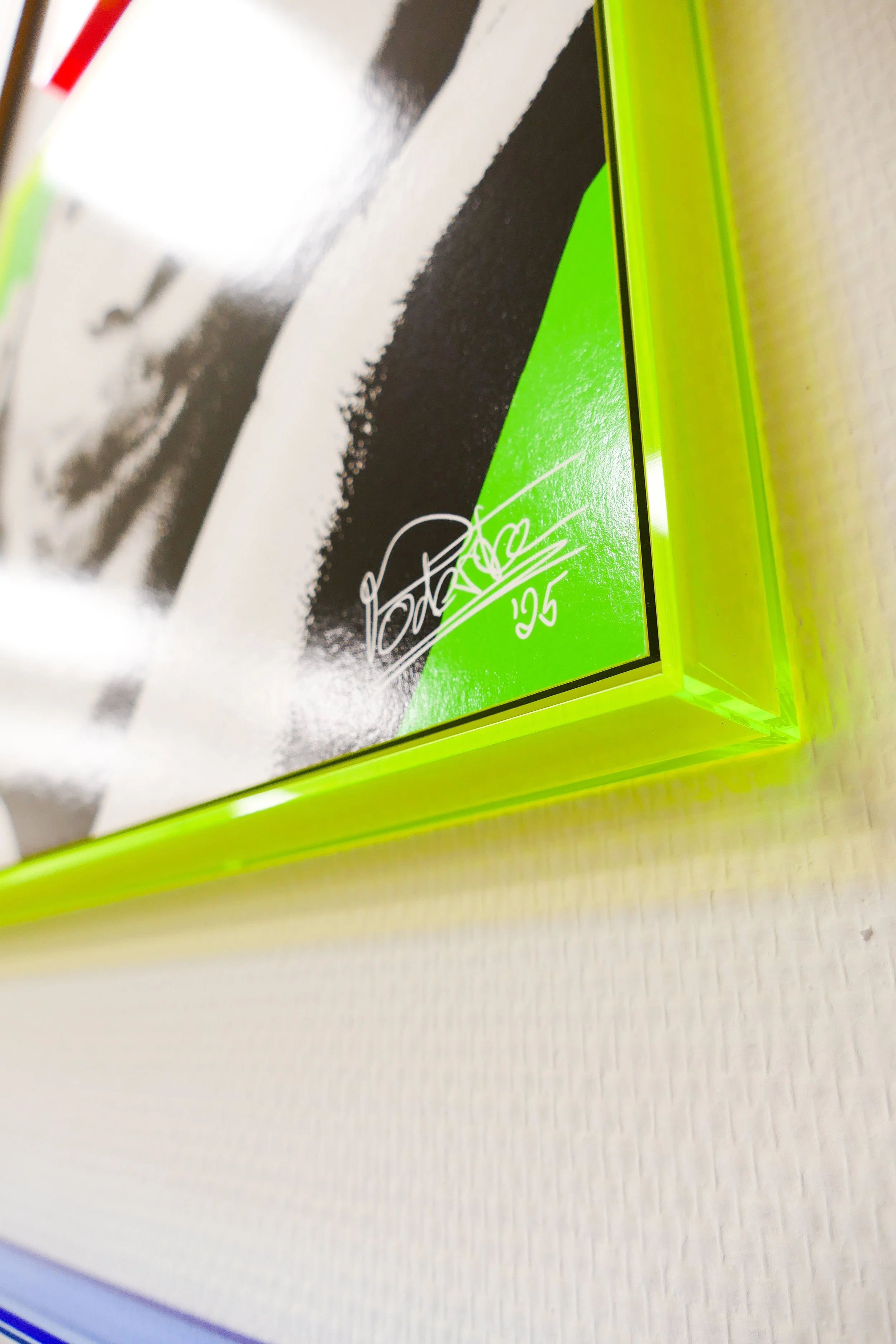 Nahaufnahme eines signierten weißen Papprahmens mit Neon-Gruen Rahmen, auf dem eine schwarze und weiße Fotografie und eine Unterschrift mit der Nummer 125 zu sehen sind.