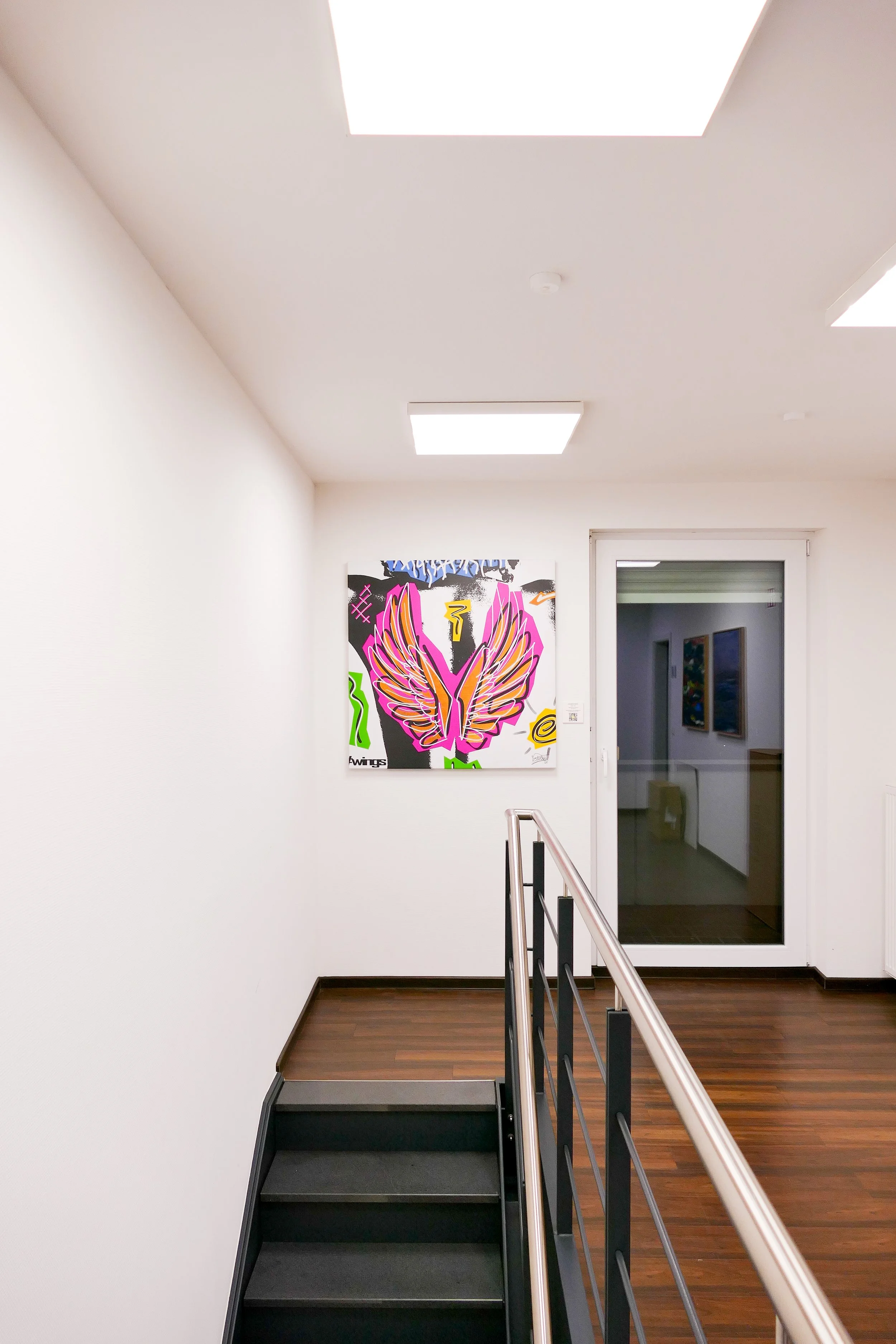 Ein weißer Flur in einer Galerie mit einem Graffiti-Britt auf der Wand und einer Glastür.