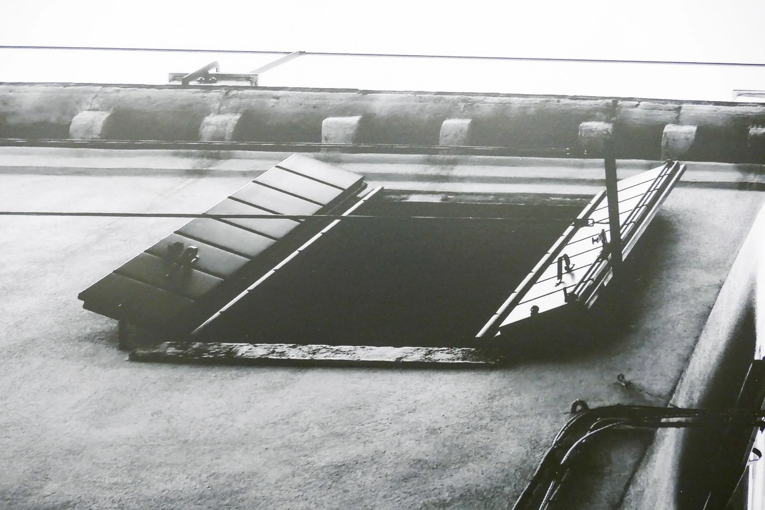 Schwarzes und silbernes Lüftungsgitter an einer Hausfassade, im Schwarz-Weiß-Foto aufgenommen.