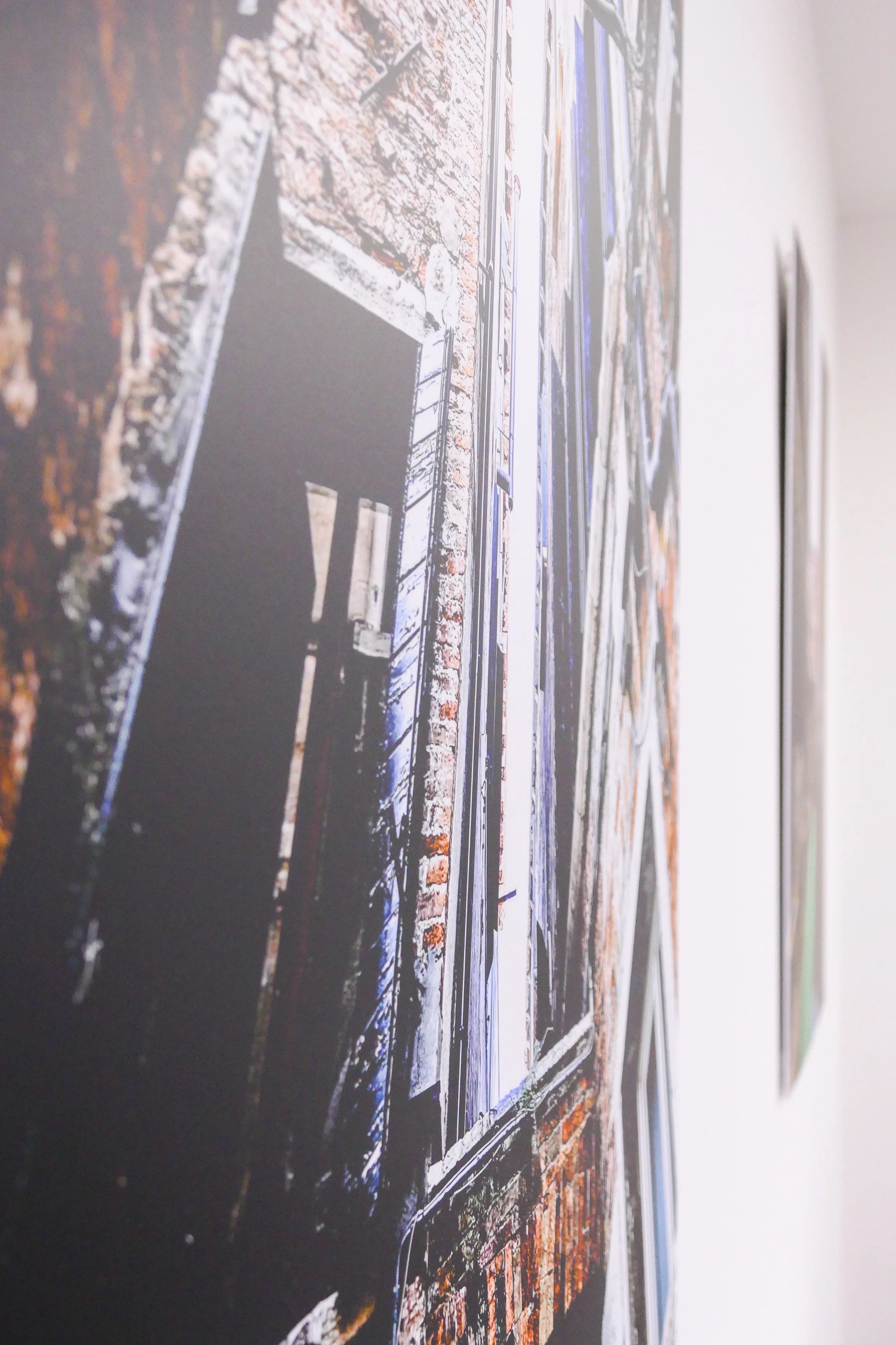 Fotografie einer Wand mit mehreren großen Kunstwerken, die im Rahmen hängen, inklusive einer großen, ausdrucksstarken Stadtbildaufnahme.