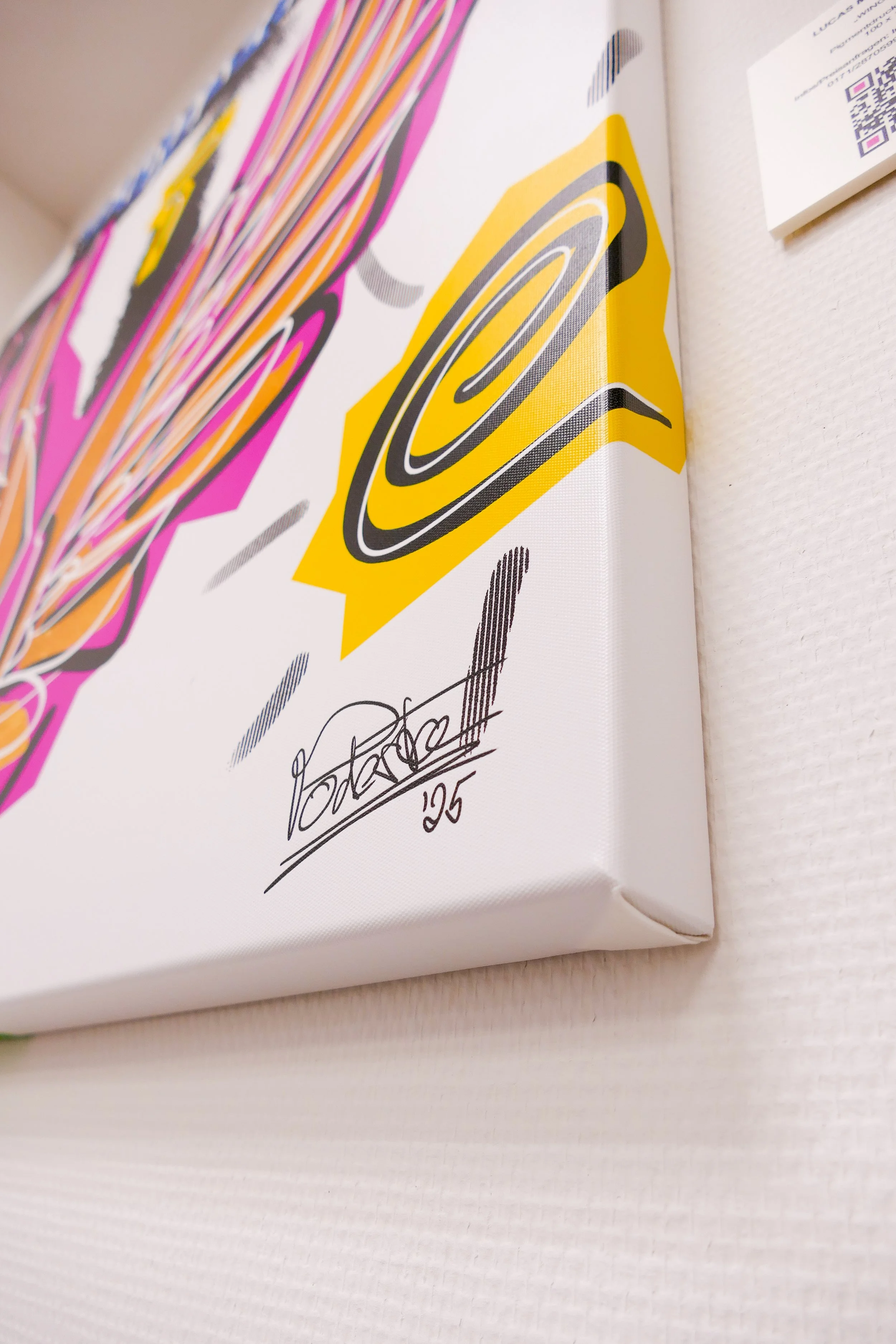 Kunstwerk mit bunten, grafischen Mustern und einem schwarzen Künstler-Signatur auf weißem Hintergrund.