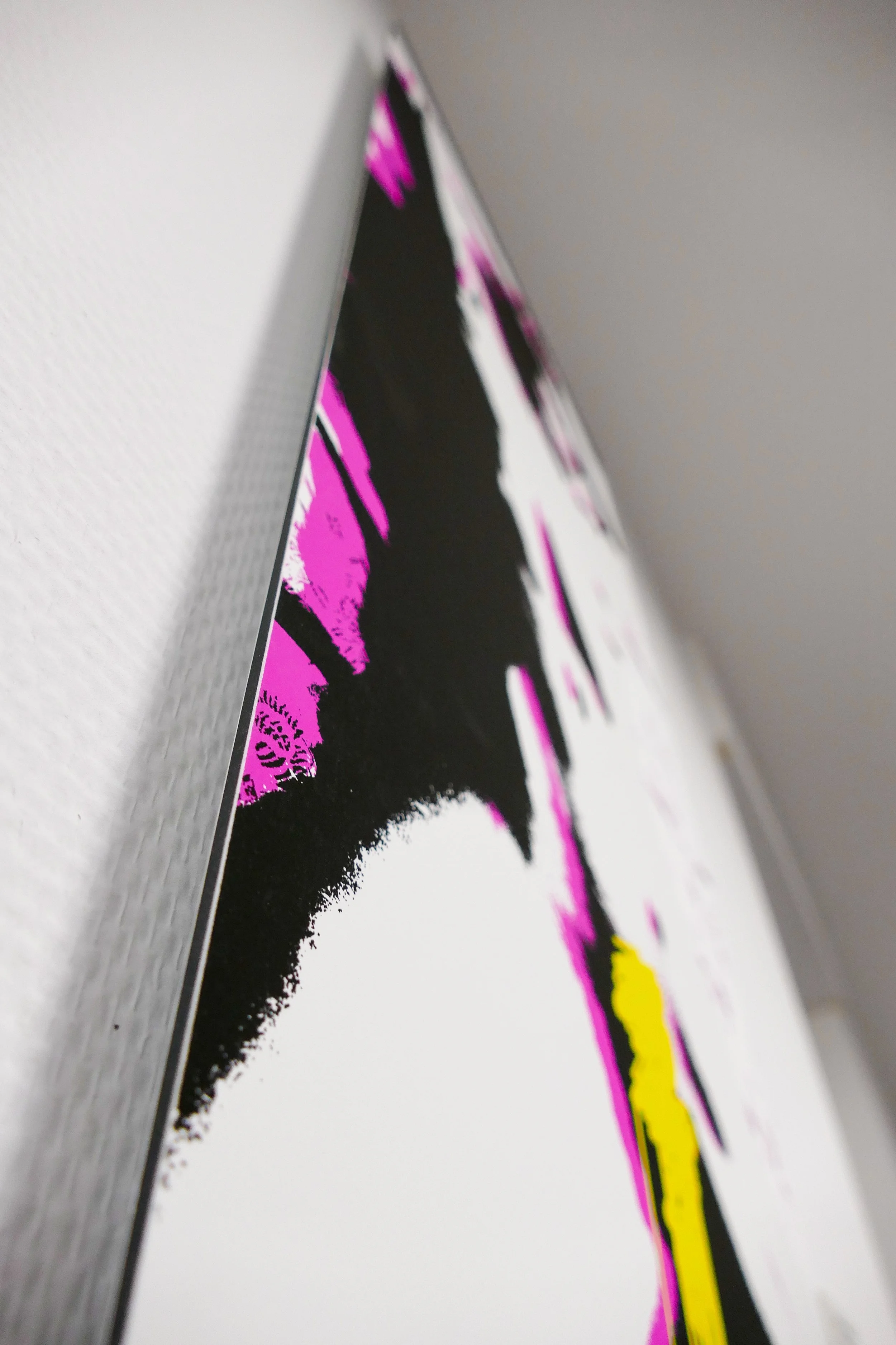 Nahaufnahme eines flachen, weißen Displays mit buntem, abstraktem Design in Pink, Schwarz und Gelb, aufgenommen aus einem seitlichen Blickwinkel.