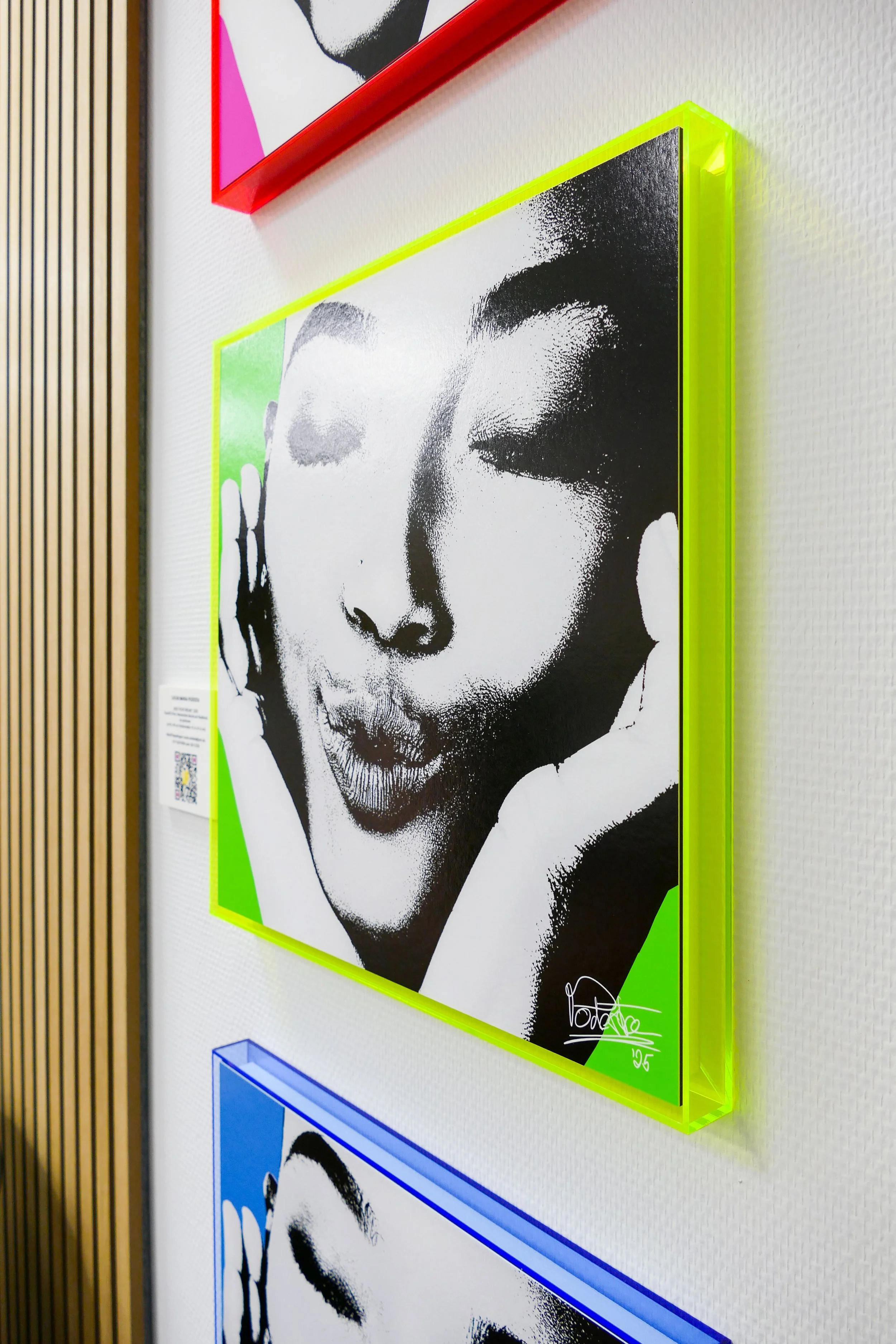 Schwarz-weiß Kunstwerk einer Person mit geschlossenen Augen, die Lippen zusammenpresst, in einem leuchtend grünen Rahmen an einer weißen Wand. Das Kunstwerk zeigt einen stilisierten, stark kontrastierenden Portrait-Style.