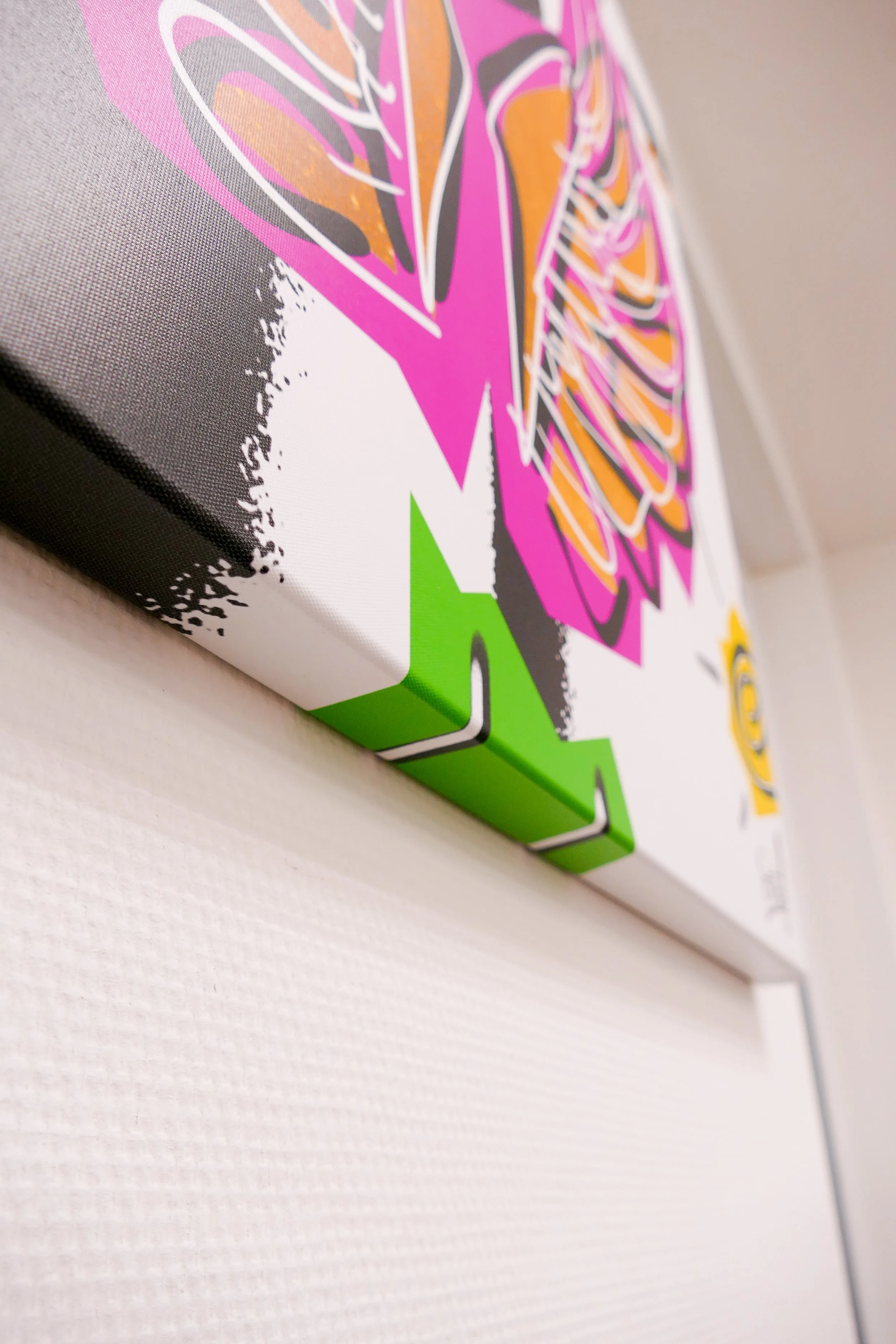 Nahaufnahme eines farbenfrohen Bildes an der Wand, das grafische, bunte Muster in Violett, Pink, Orange, Schwarz, Weiß und Grün zeigt.