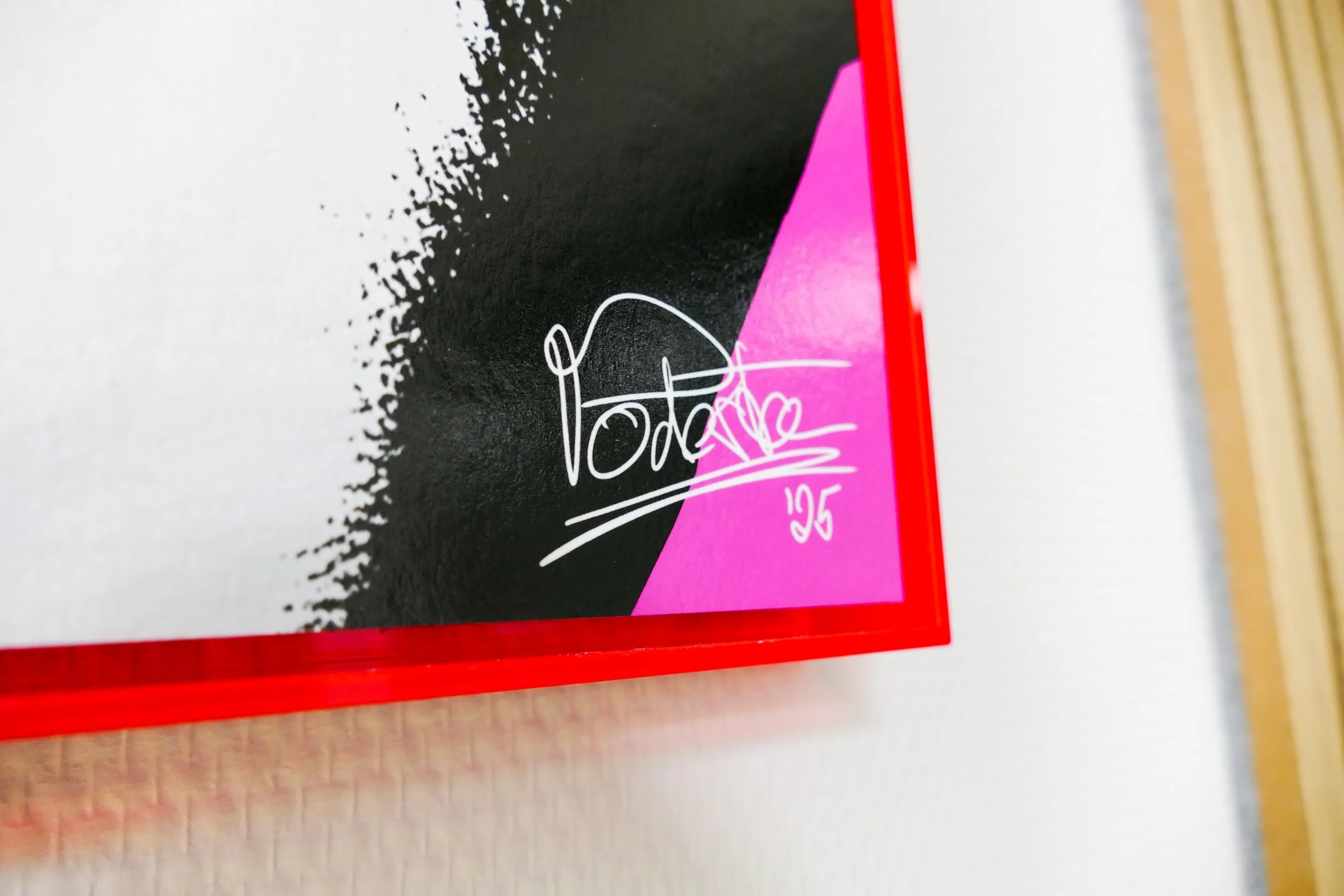 Ein Fußball mit einer Signatur und der Nummer 25, auf einem pinken und schwarzen Hintergrund, eingerahmt mit einer roten Leiste.