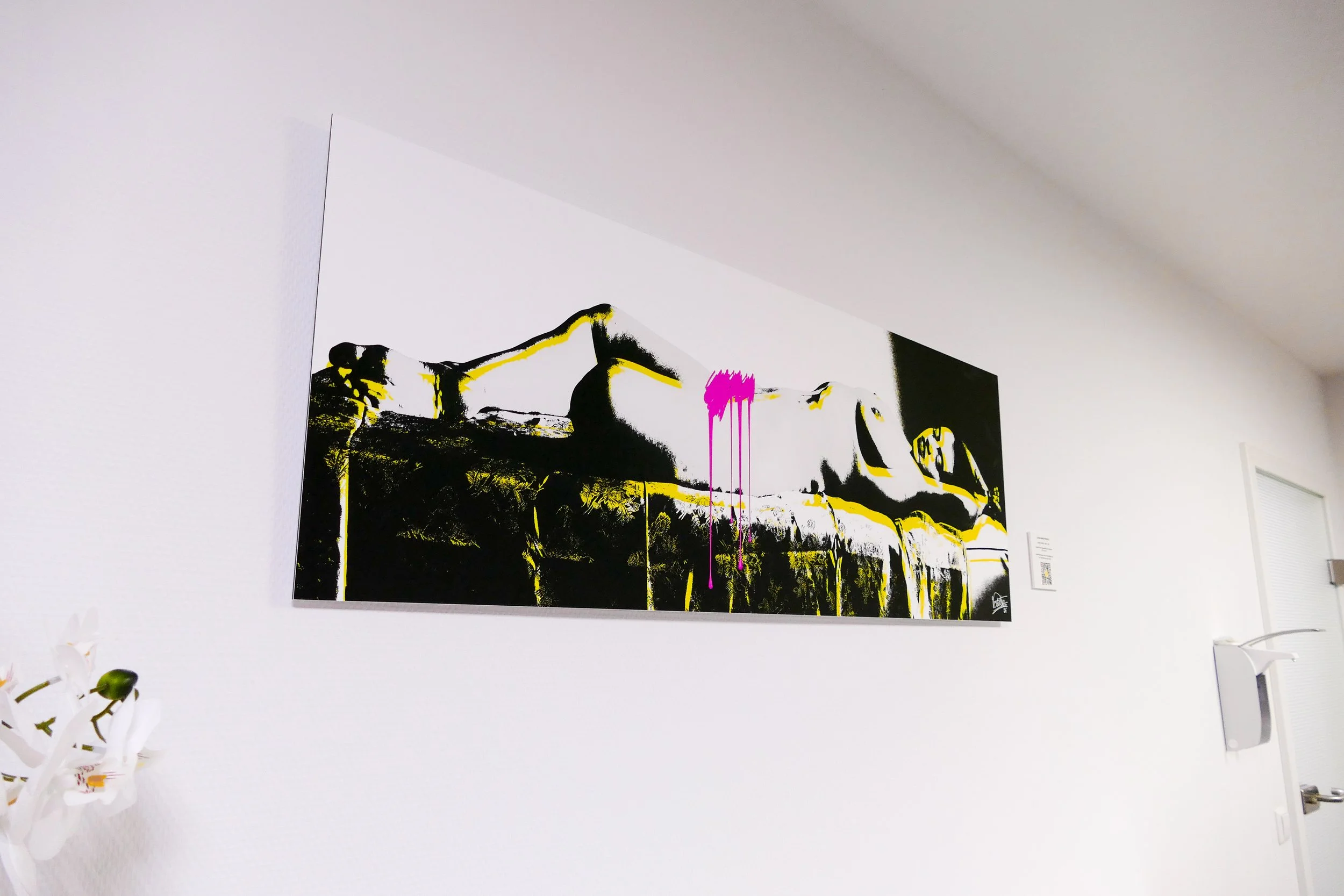 Moderner Street-Art-Gemälde an einer weißen Wand, zeigt eine stilisierte, schwarz-weiße Frauenfigur mit gelben Akzenten und pinken Farbtropfen in der Mitte.