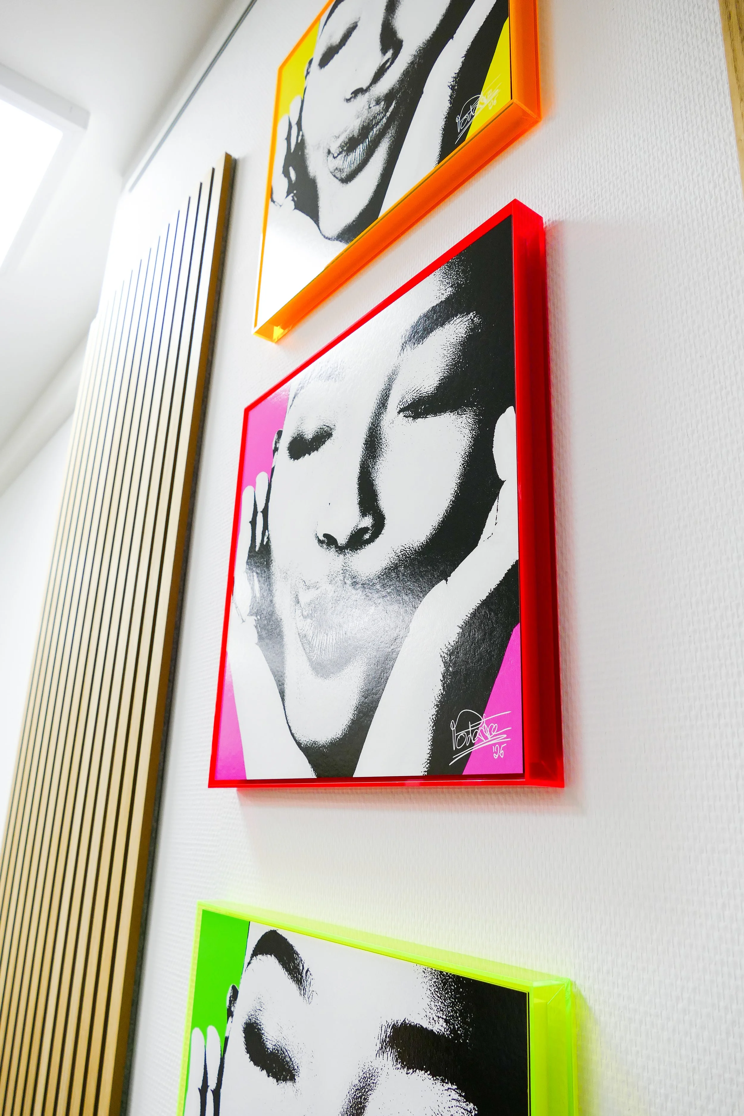 Drei stylisierte Porträtbilder in modernen Rahmen an einer weißen Wand, mit einer Holzvertäfelung daneben.