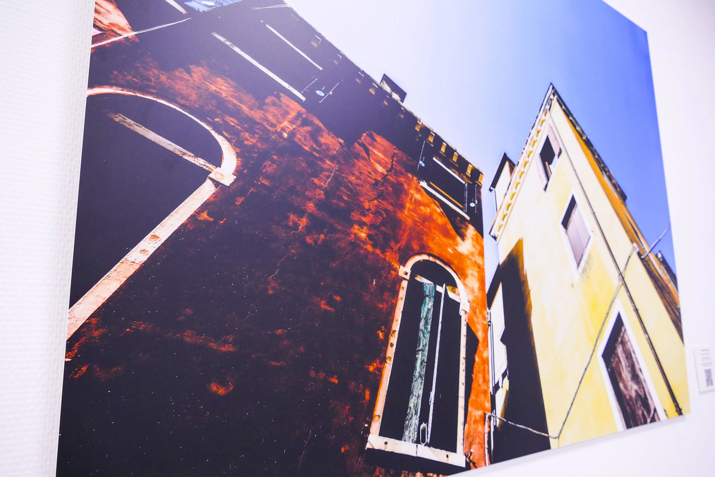 Foto von einem Parkplatz mit leeren Parkplätzen, einer gelben Gebäudefront auf der rechten Seite und einem blauen Himmel im Hintergrund.