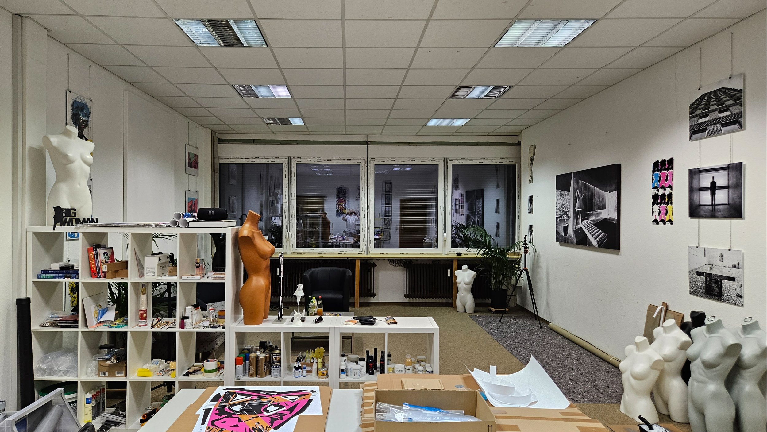 Kunstatelier mit Skulpturen, Regalen, Malerei, bemalten Mennekes, Malpinseln, leeren Männergipsen, Wandbildern, Pinsel, Farben und Zeichenmaterialien.