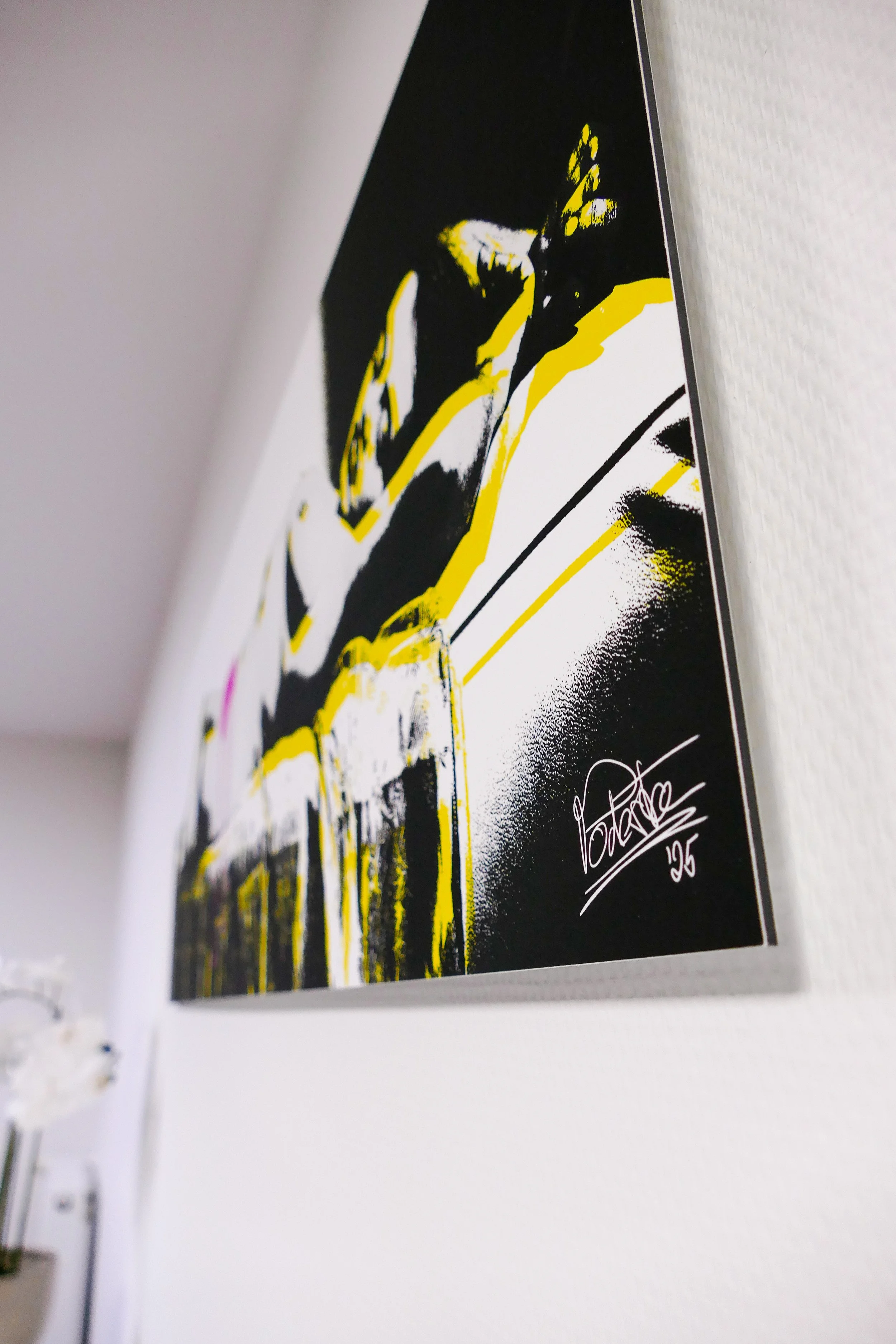 Kunstwerk an der Wand mit einer Signatur und der Jahreszahl 25, in Schwarz, Weiß und Gelb gehalten.