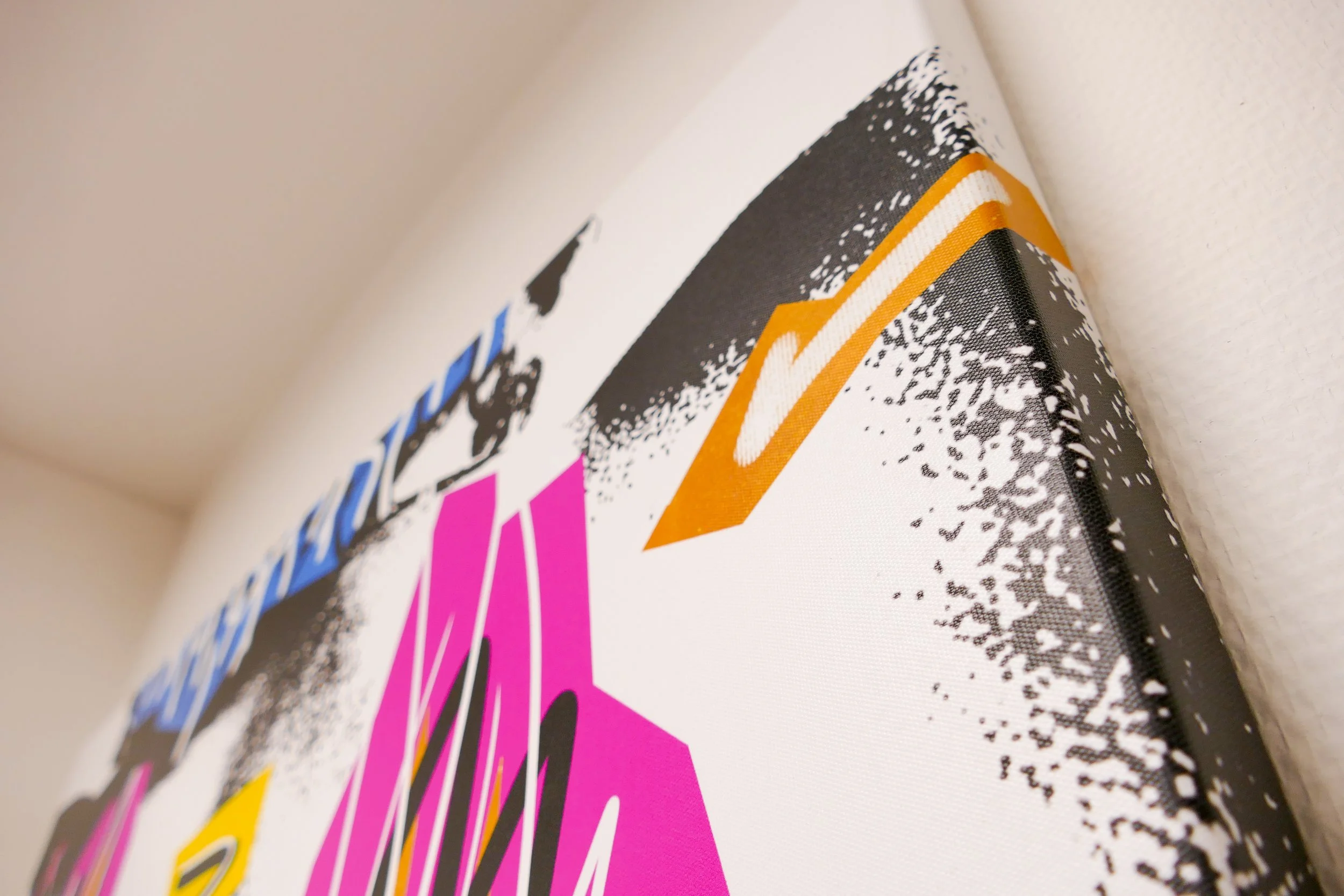 Nahaufnahme eines bedruckten Canvas-Bildes mit bunten Schriftzügen und grafischen Elementen, das an der Wand hängt.