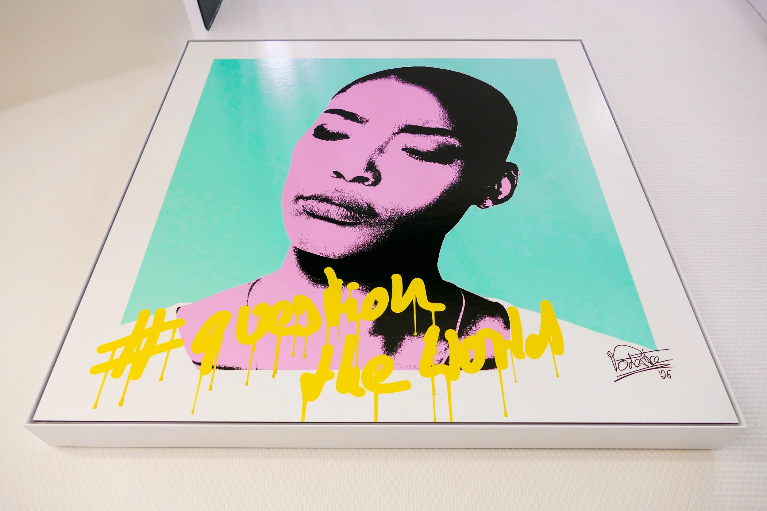 Kunstwerk eines Porträts einer Frau mit geschlossenen Augen, in Neonfarben, mit gelber Graffiti-Schrift darunter, die #1 obsession the world lautet, signiert in der unteren rechten Ecke.