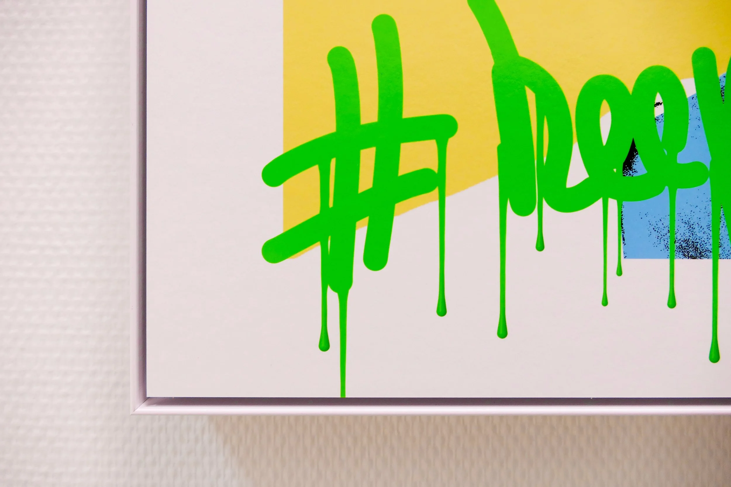 Graffiti-Kunstwerk mit grünem Tag auf einer Wand, teilweise verdeckt durch eine Ecke eines Rahmens, mit blauer und gelber Hintergrundfarbe.