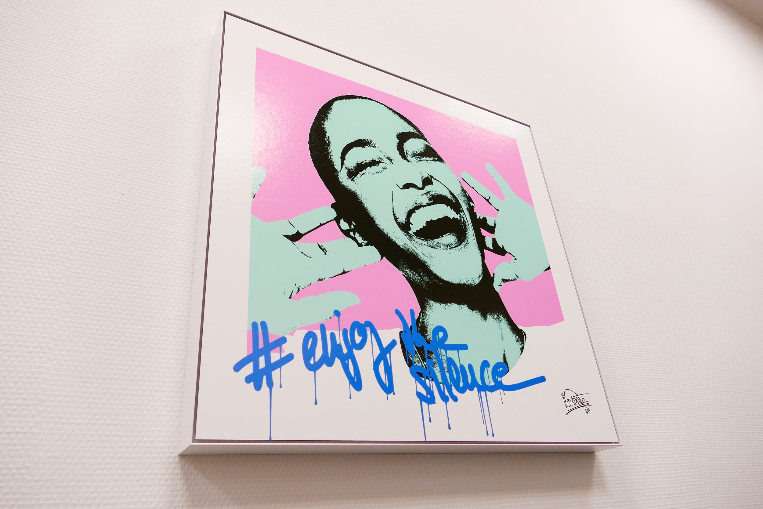 Street Art Bild einer lachenden Frau mit offenem Mund und geschlossenen Augen, im Pop Art Stil mit pinkem, blassem und blauen Farbgebung, inklusive Graffiti-Schriftzug '#enjoy the silence'.