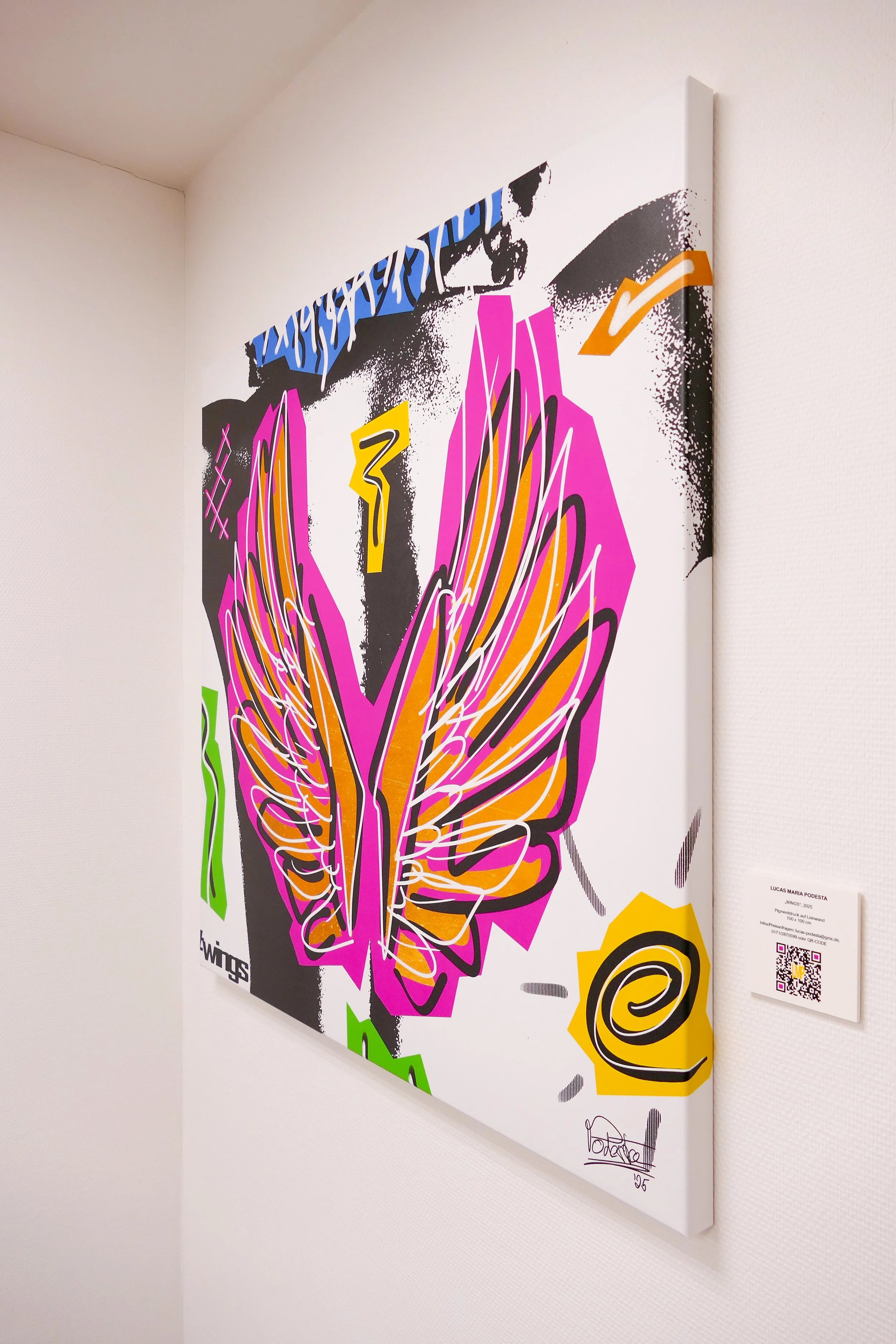 Farbiges abstraktes Kunstwerk mit Flügel-Design und verschiedenen grafischen Elementen an einer weißen Wand.