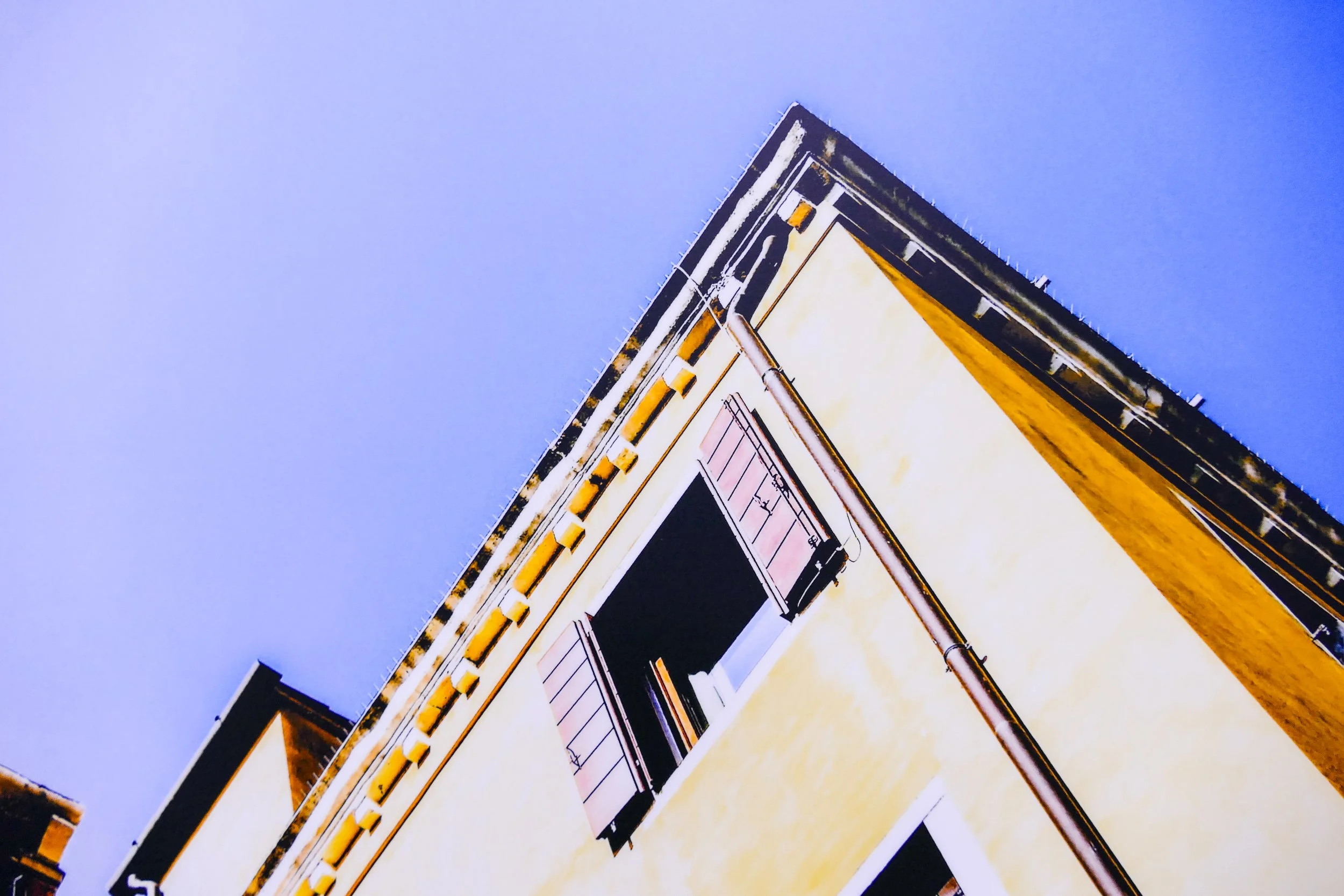 Blick auf die Ecke eines gelben Gebäudes mit einem Balkon und einer blauen Himmel im Hintergrund.