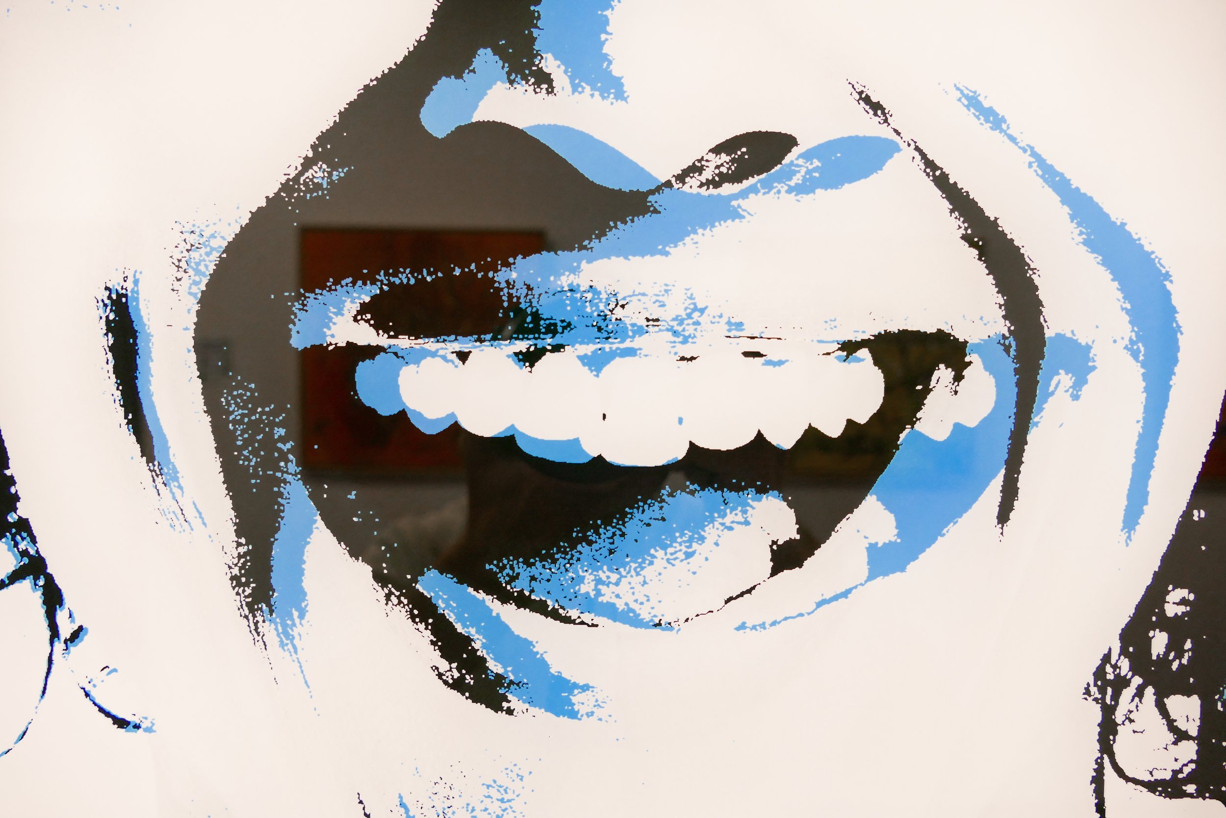 Streetart-Druck eines lachenden Gesichts in Schwarz, Weiß und Blau, mit einem offenen Mund, auf einer weißen Wand.