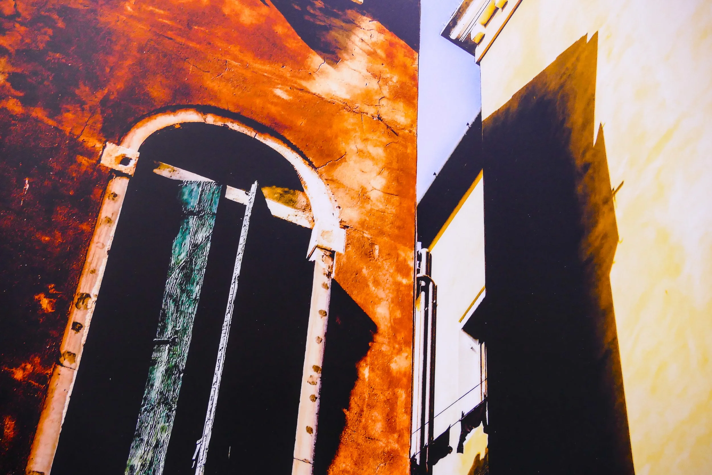 Fotografie eines alten, verzierten Türbogens an einer roten Wand, daneben ein weißes Gebäude mit Schatten