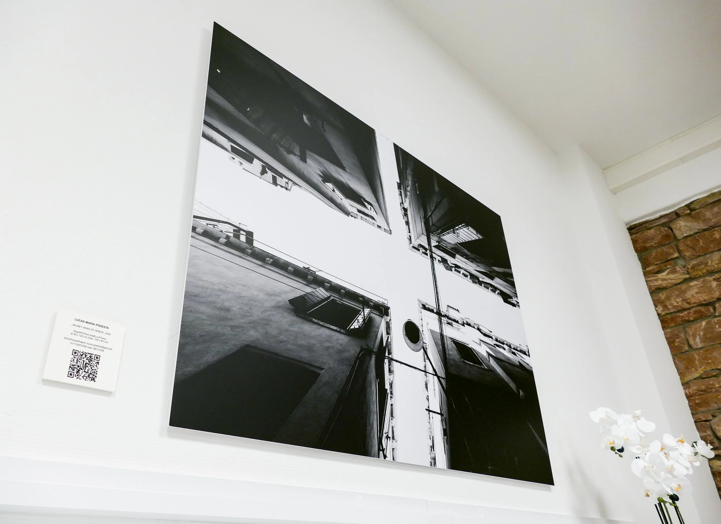 Schwarz-Weiß-Fotografie eines Innenhofs mit mehreren Gebäuden, aufgenommen aus einer niedrigen Perspektive, Blick nach oben, sichtbare Fenster und Mauern.