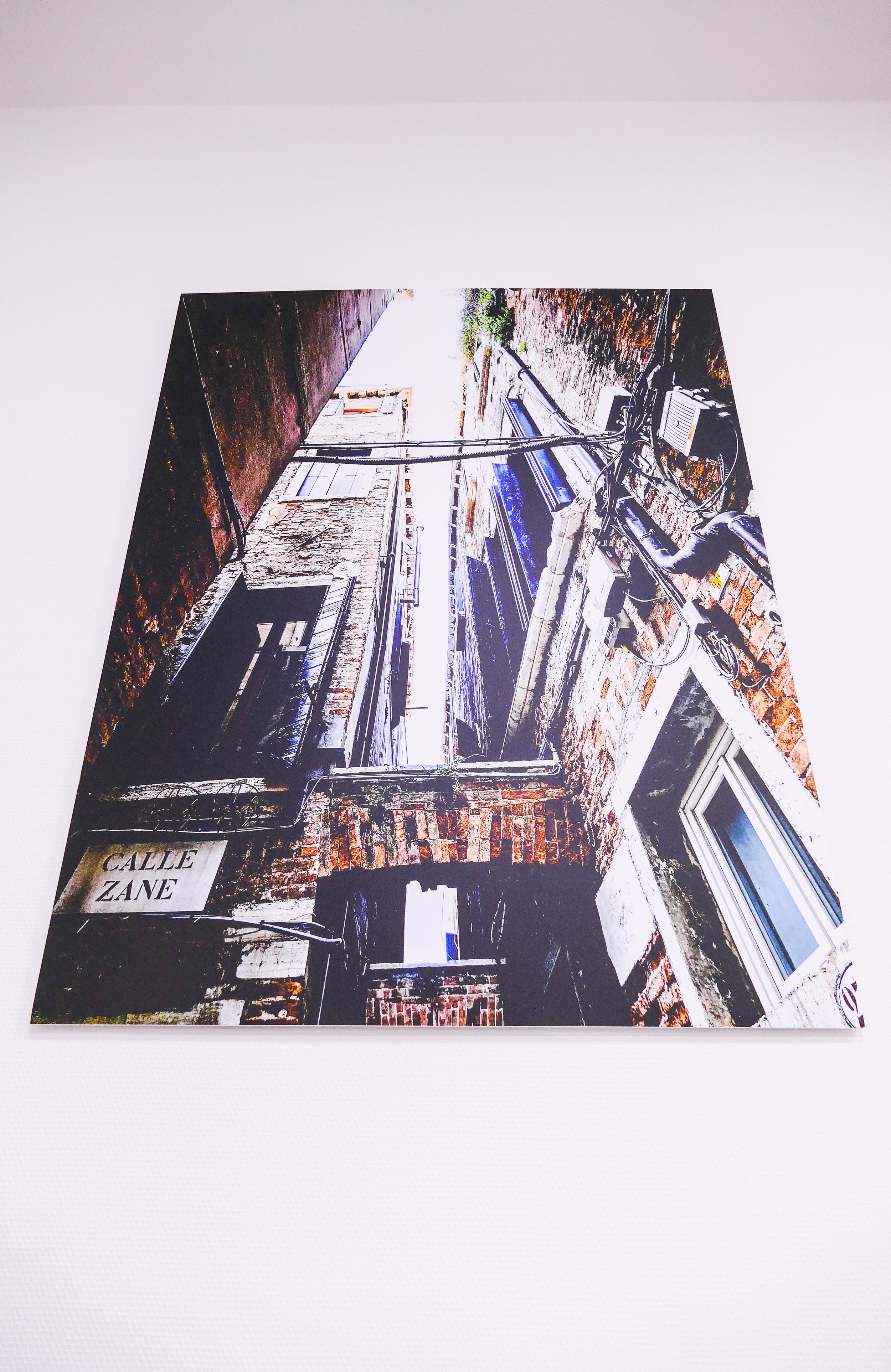 Gemälde einer dunklen, verlotterten Gebäudefassade mit einer Schilder mit der Aufschrift »Calle Zane« und mehreren Fenstern, Kabeln und Rohren.