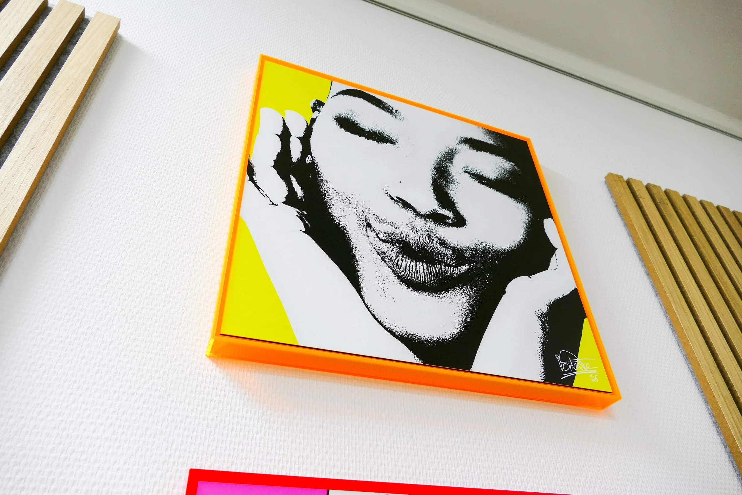 Schwarz-weiß Portrait eines lachenden Mädchens mit geschlossenen Augen, umrahmt von einem orangefarbenen Rahmen, auf einer gelben Ecke auf einer weißen Wand.